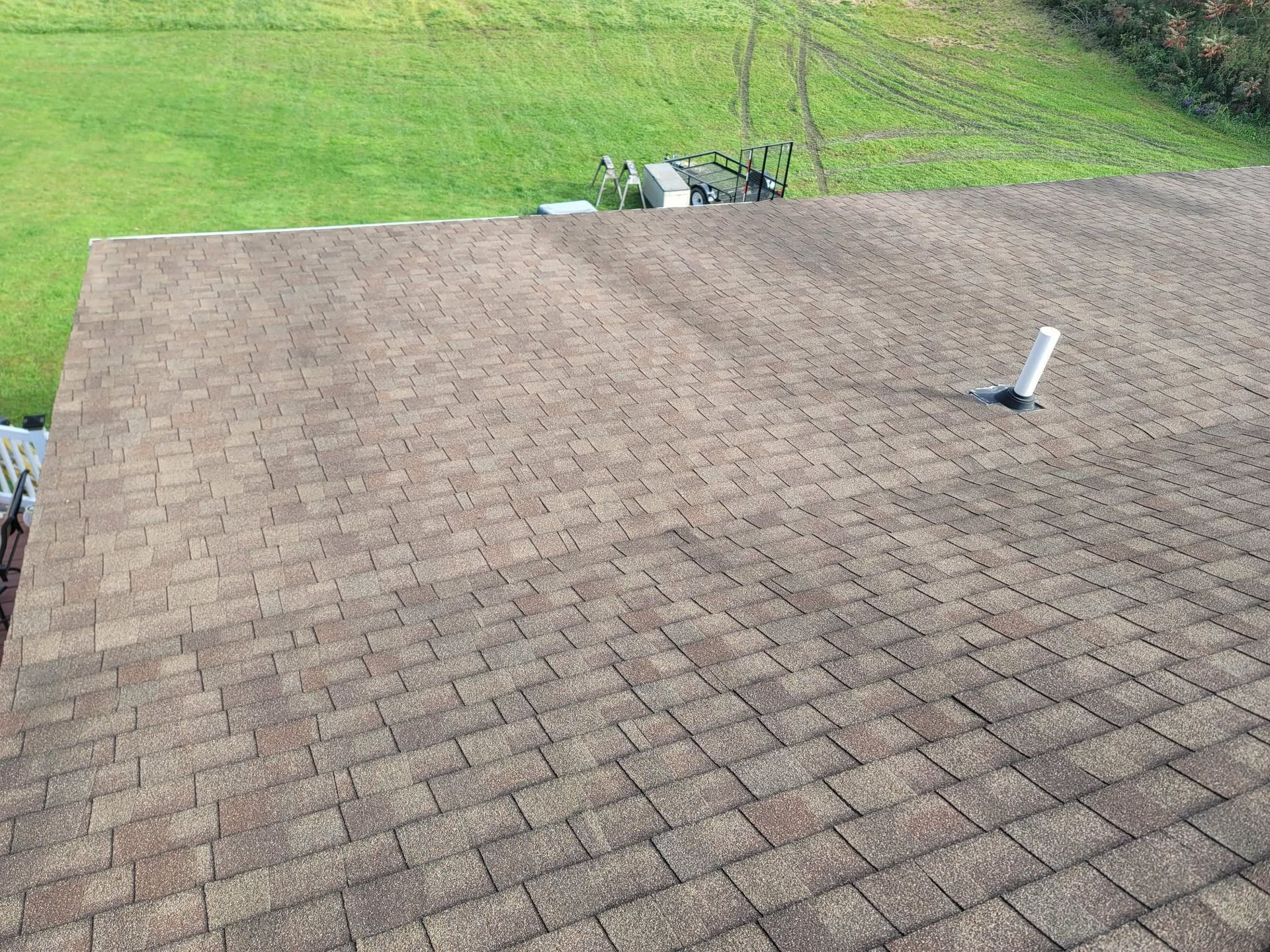 Brown shingled roof with a vent pipe, bordered by green lawn in the background