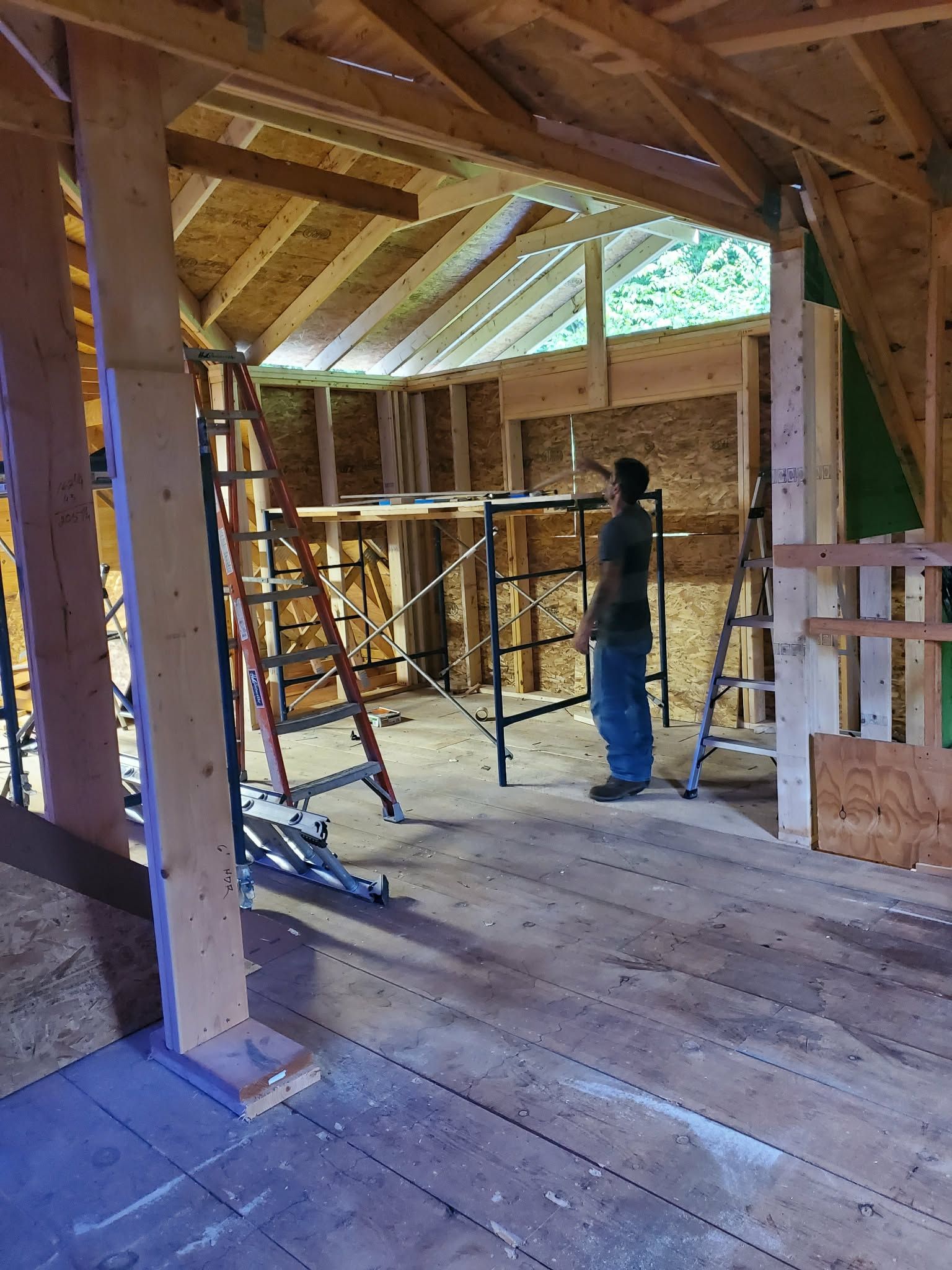 Worker inside unfinished wooden attic with exposed rafters and scaffolding during construction