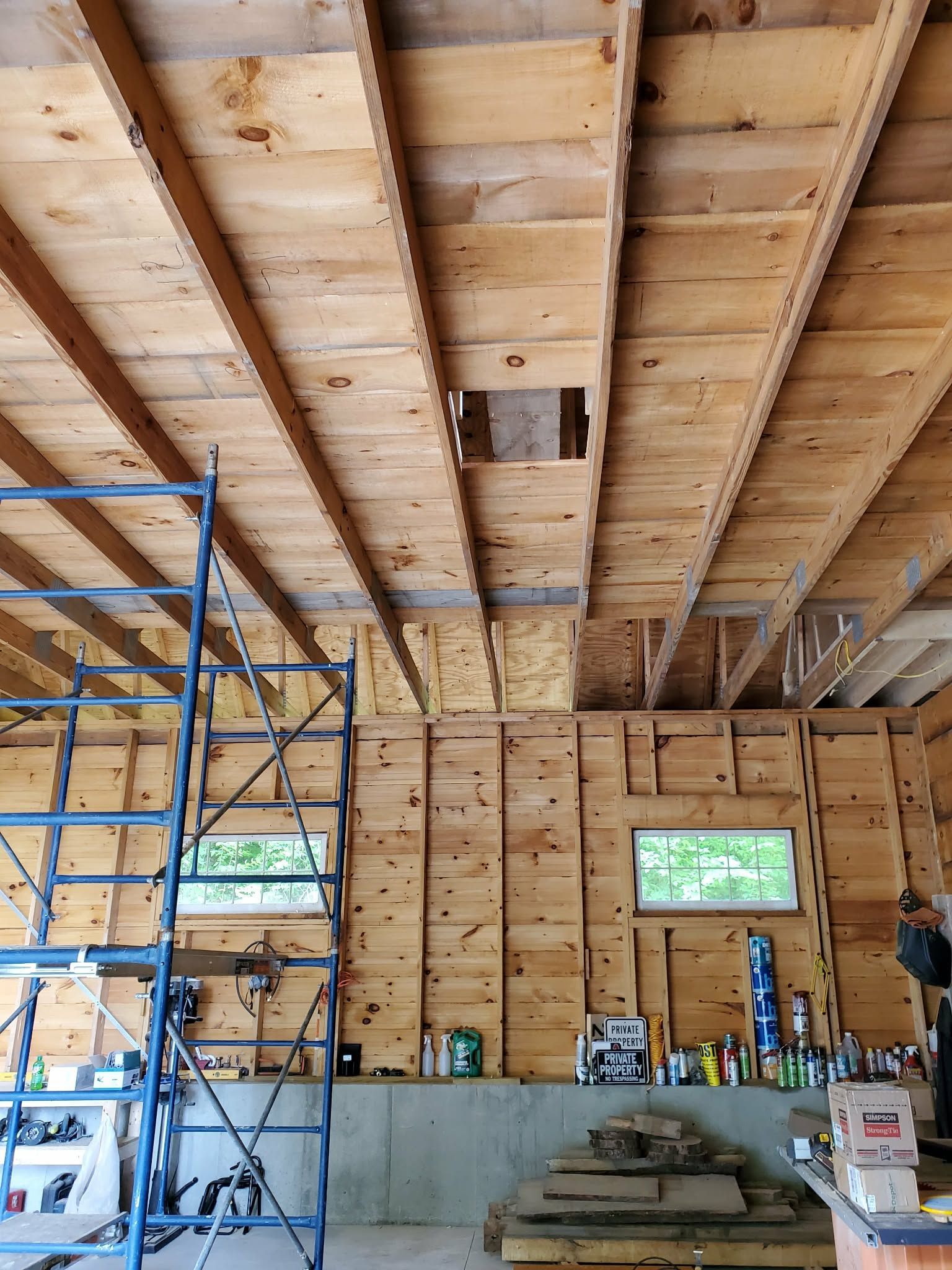 Wood-framed interior under construction with scaffolding, exposed rafters, and building materials stacked inside.