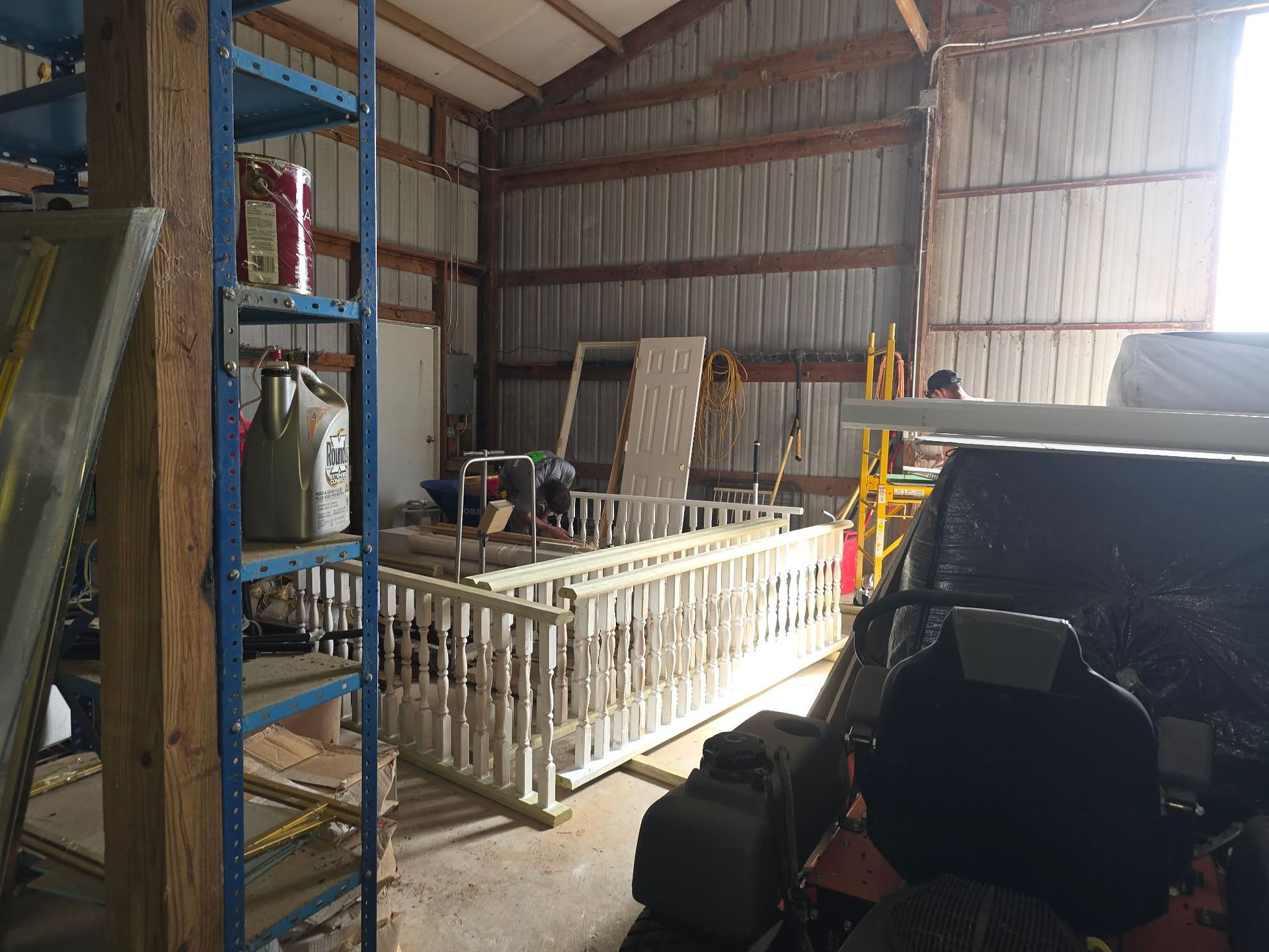 Indoor warehouse with shelves, equipment, and a white railing, lit by sunlight from a large open door