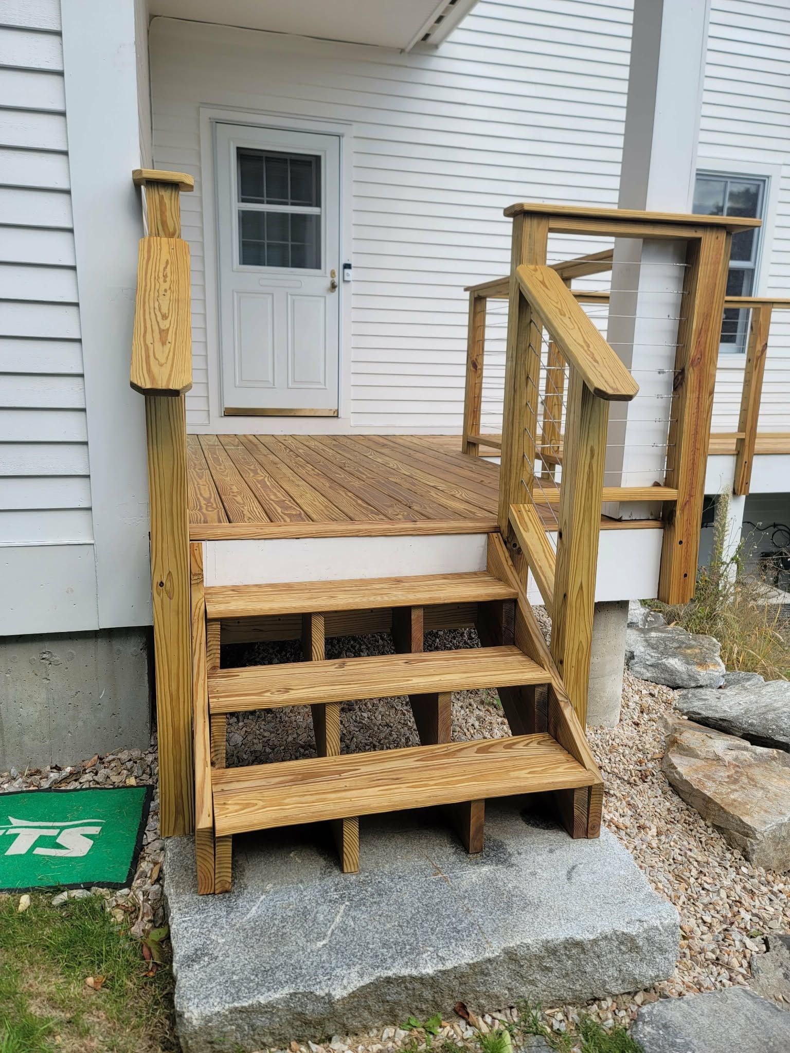 Wooden stairs and porch railings leading to a white house entrance with a front door.