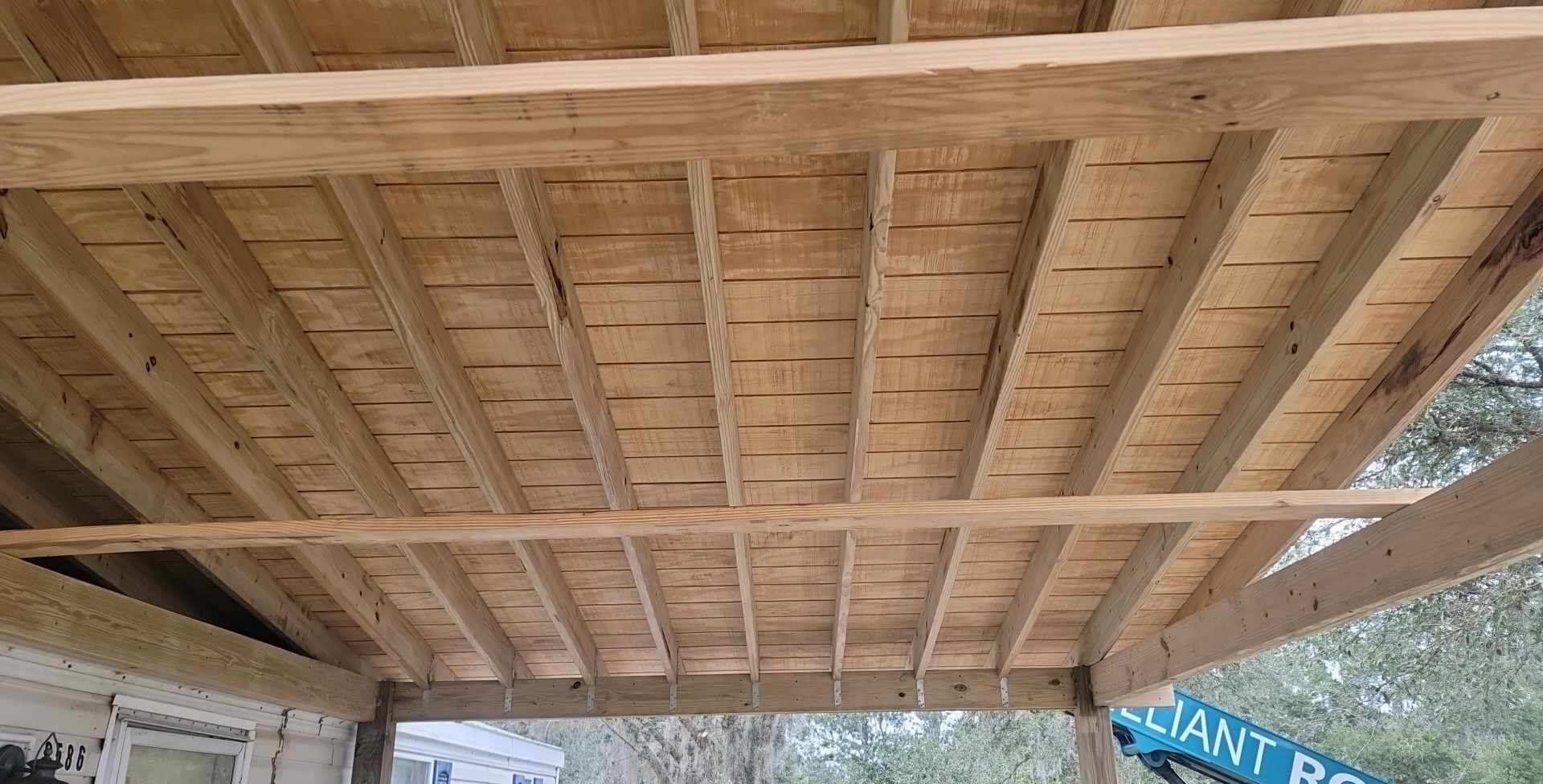Wooden plank ceiling under construction, viewed from below with exposed beams and daylight at the edge.