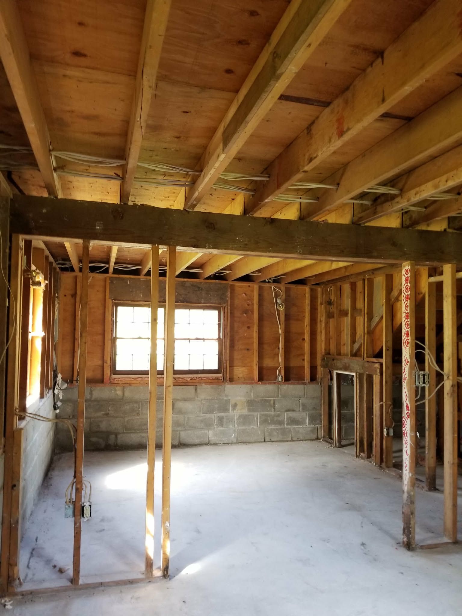 Unfinished room with exposed wooden studs, ceiling joists, cinder block wall, and concrete floor.