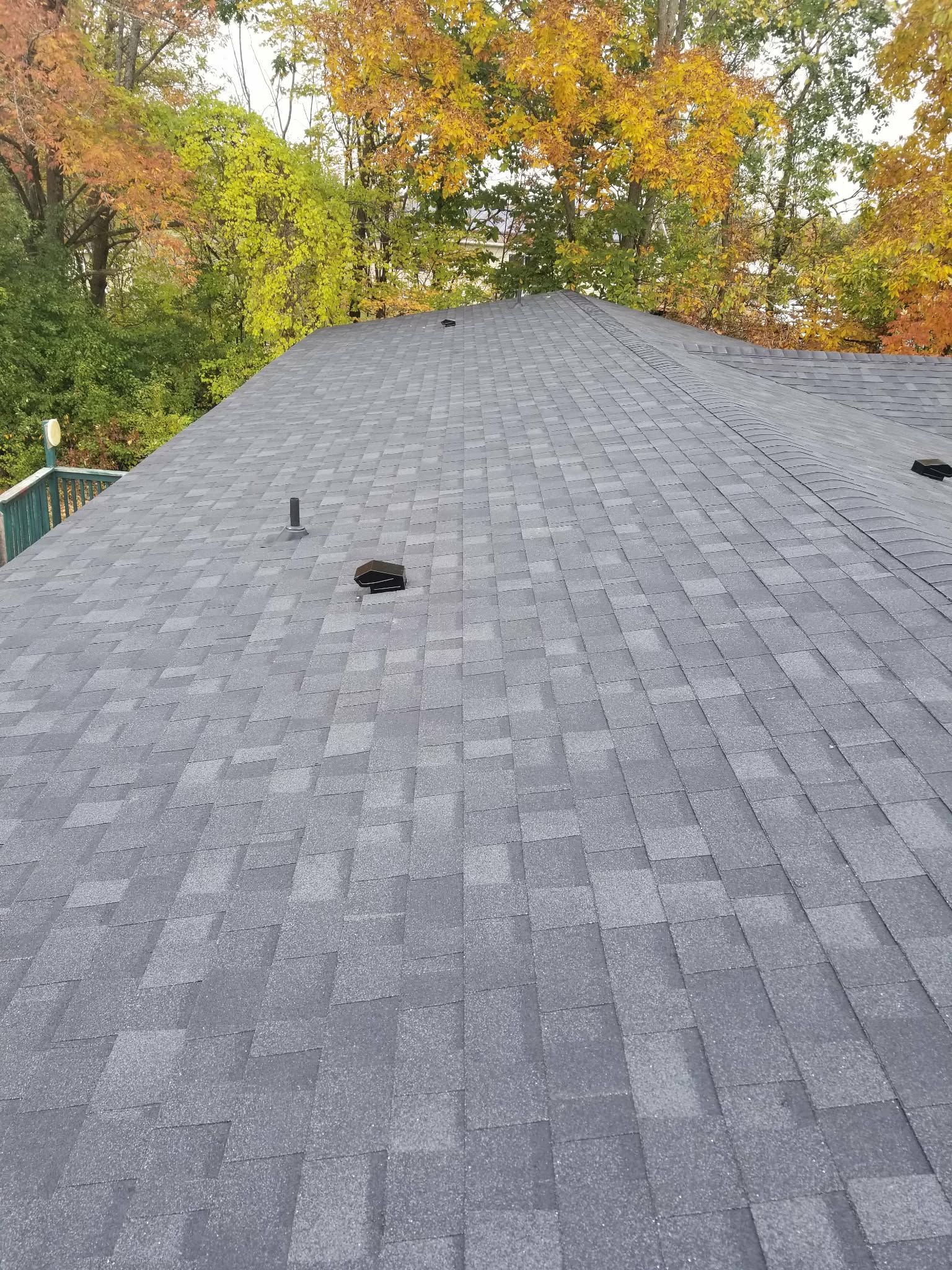 Gray shingle roof with vents, seen from above, with autumn trees in the background