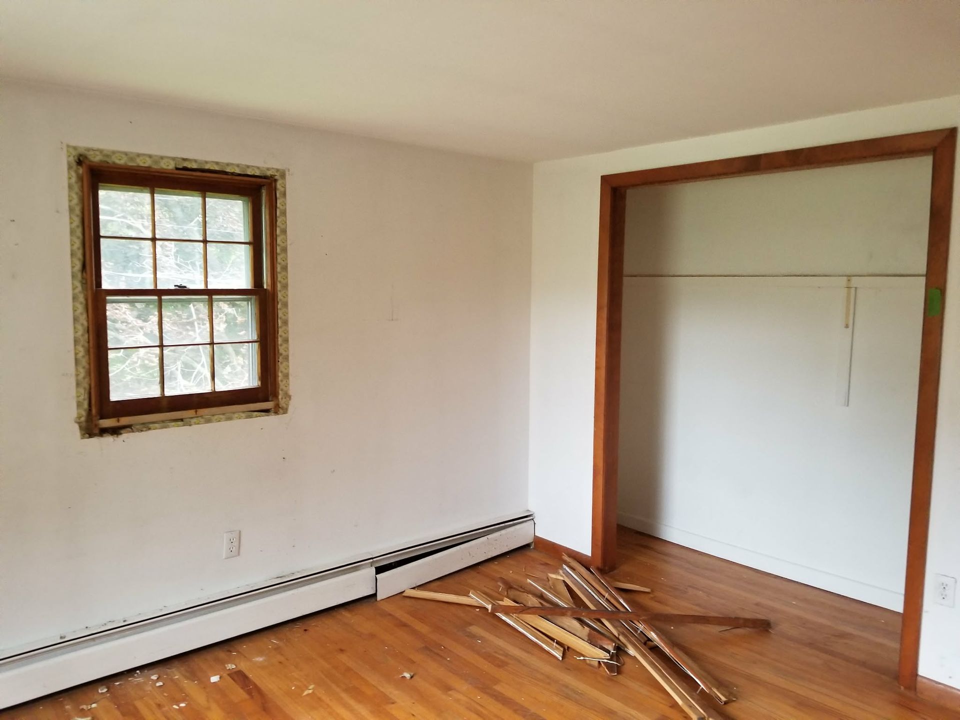 Empty room with white walls, wood trim, a small window, and construction debris on the floor.