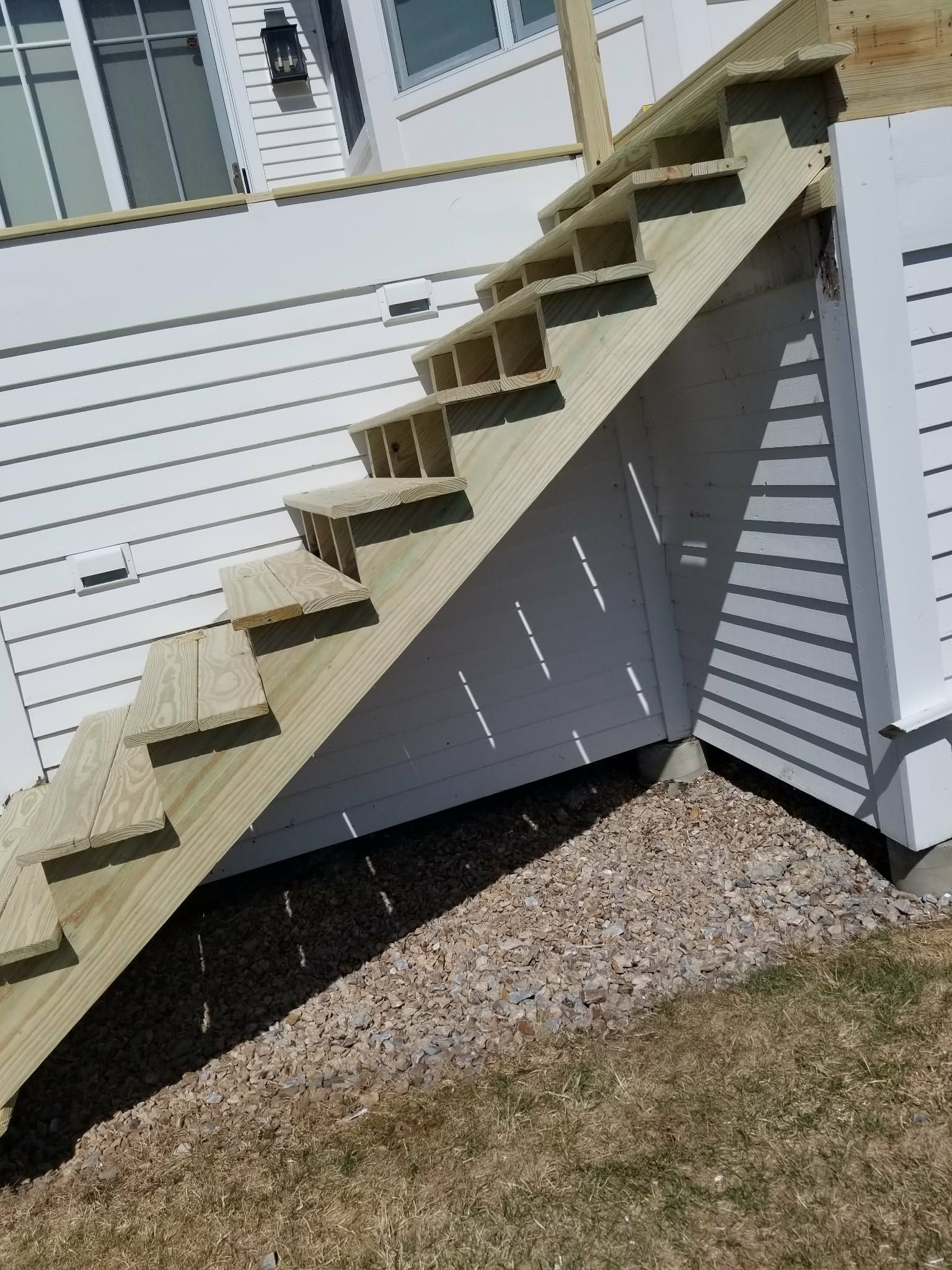 Outdoor wooden staircase attached to a white house over a gravel bed