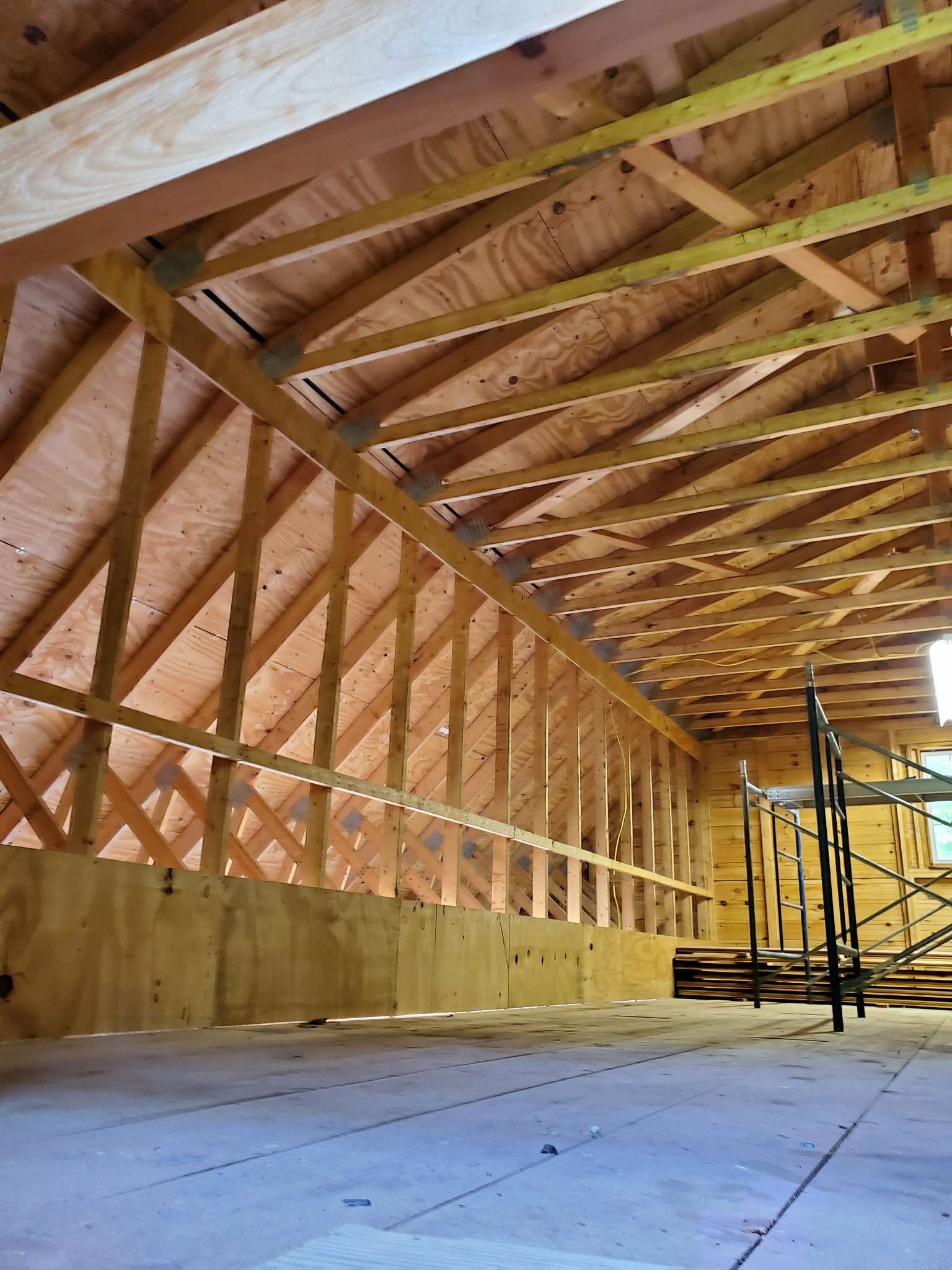 Interior of a wooden barn under construction, with roof trusses, wall framing, and scaffolding.