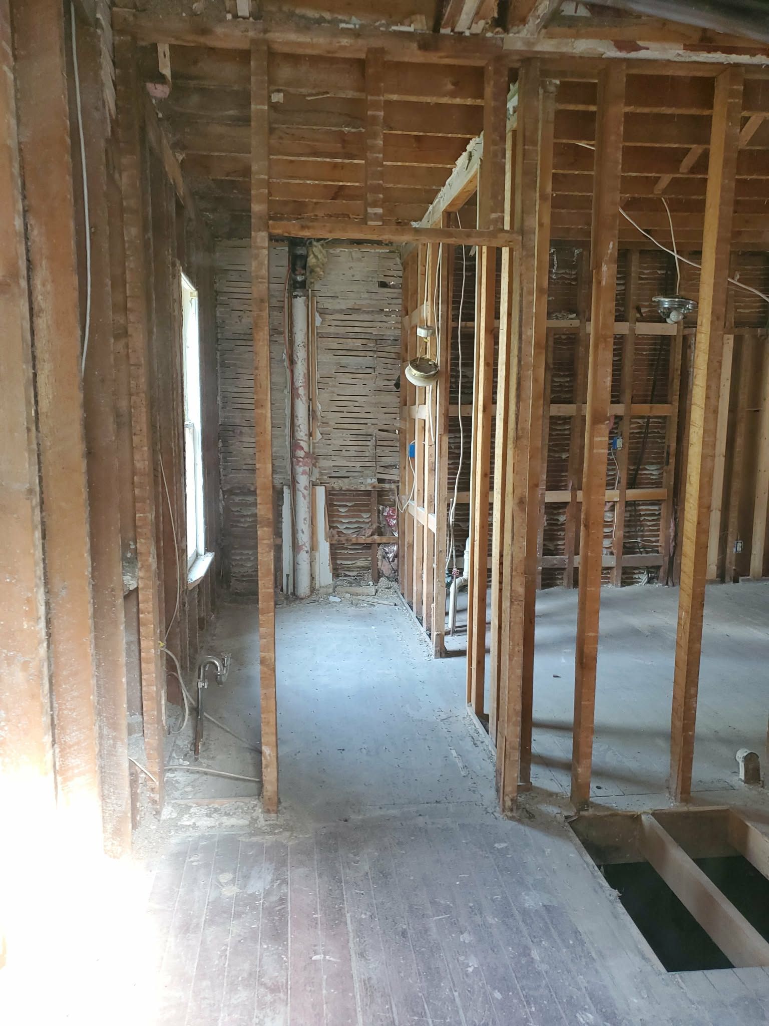 Unfinished interior with exposed wooden studs, brick wall, and concrete floor under construction