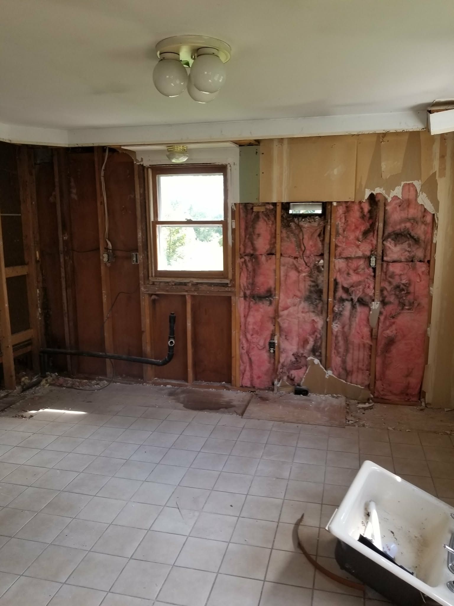 Partially demolished room with exposed insulation, tiled floor, and a small window.