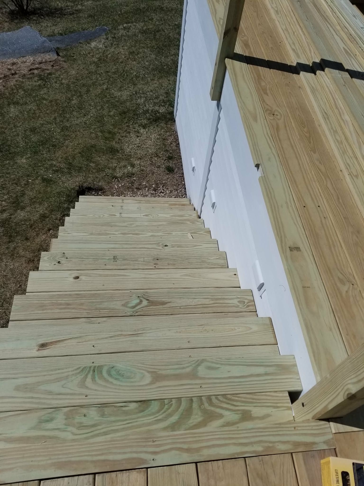 Wooden staircase beside white house siding leading down to a grassy yard