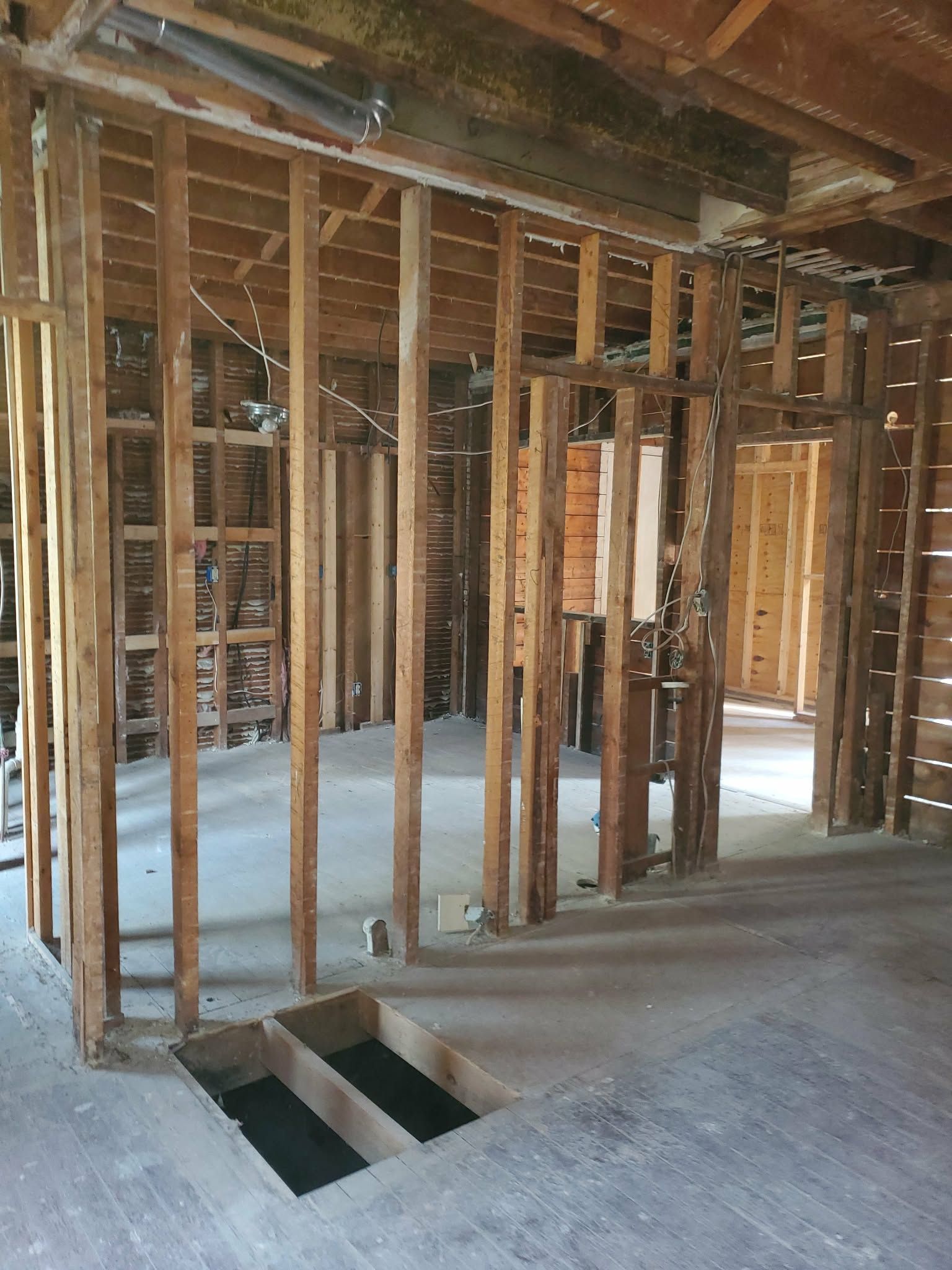 Interior under renovation with exposed wall studs, unfinished floor, and a stair opening.