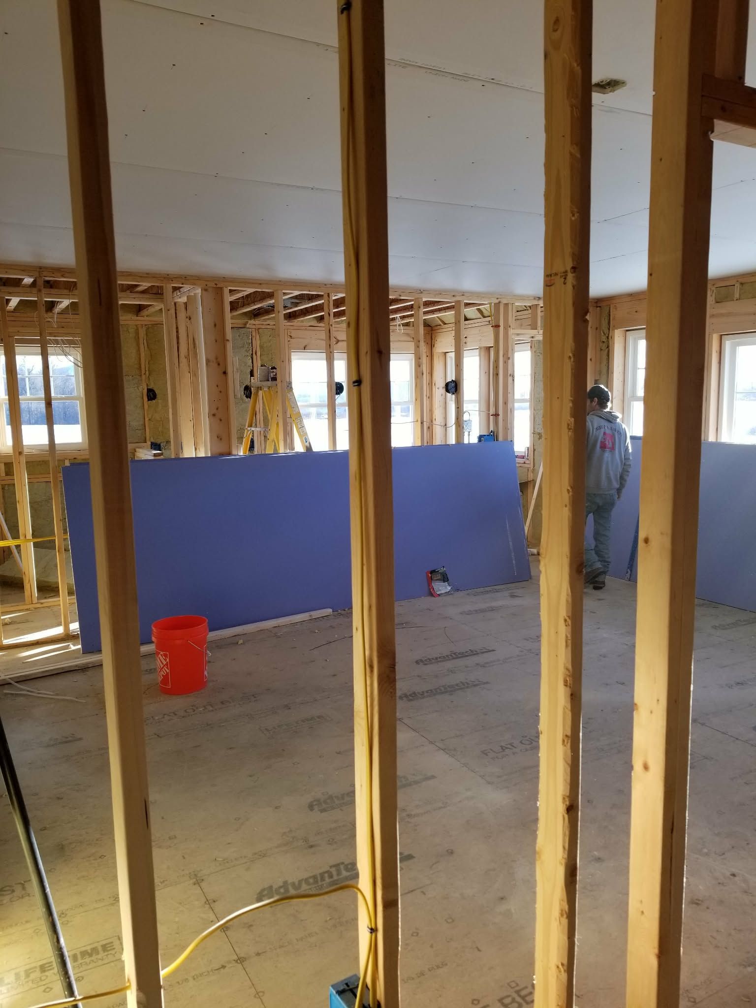 Interior of a wood-framed construction site with blue barrier panels and a red bucket on the floor