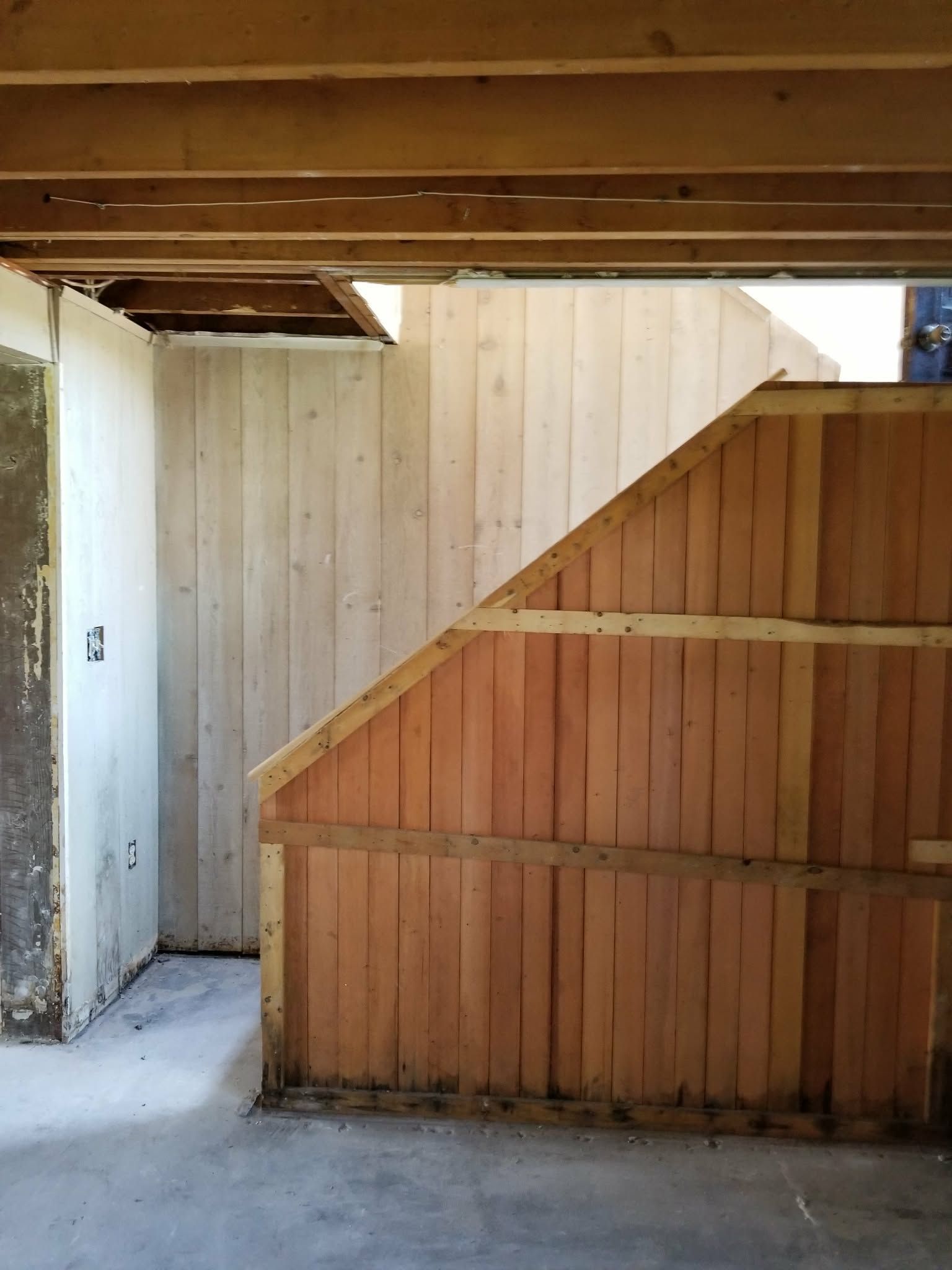 Wooden fence and gate under a covered outdoor structure, with a white wall on the left.