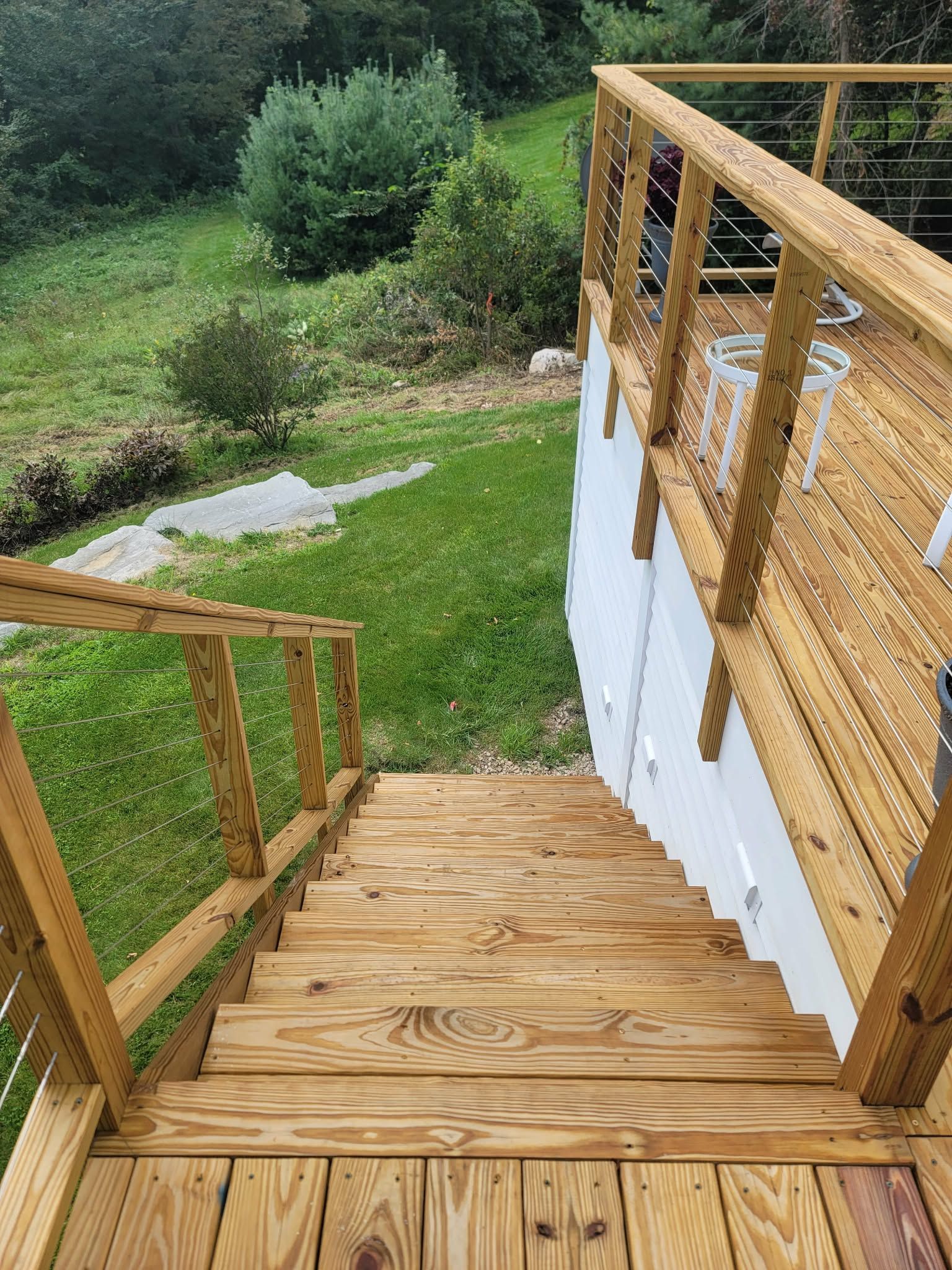 Wooden outdoor staircase with railing leading down to a grassy yard and trees beyond.