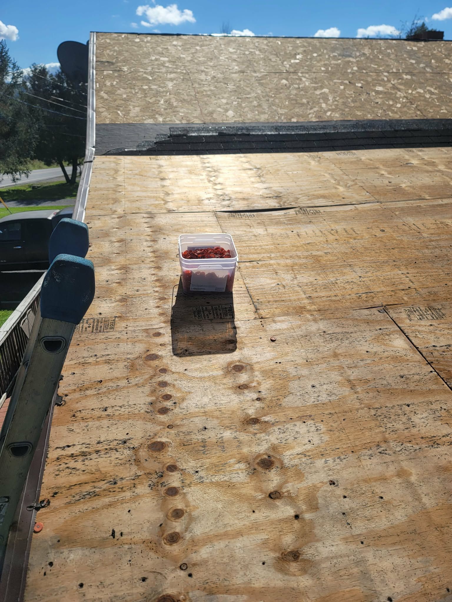 Roofing work on a steep plywood roof with a single shingle bundle near the center