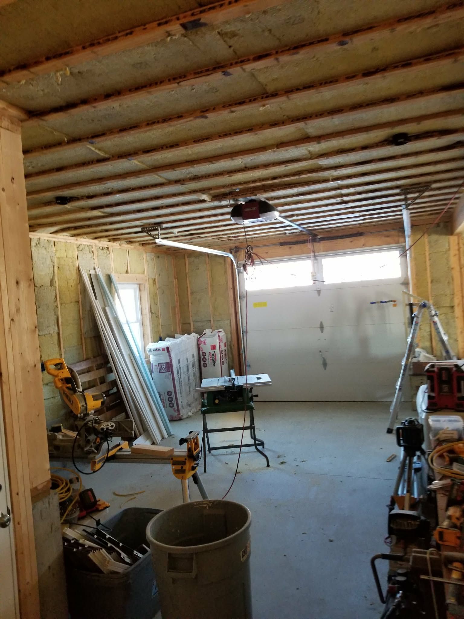 Unfinished garage interior with exposed beams, tools, ladder, workbench, and a closed white garage door.