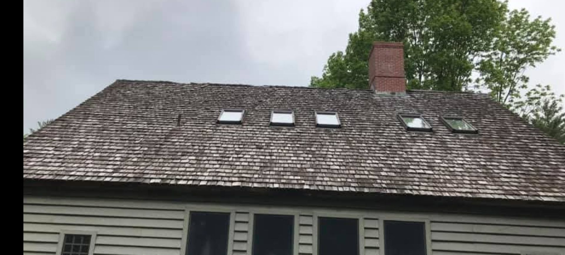 Gray shingled roof with four skylights and a red brick chimney above a house exterior