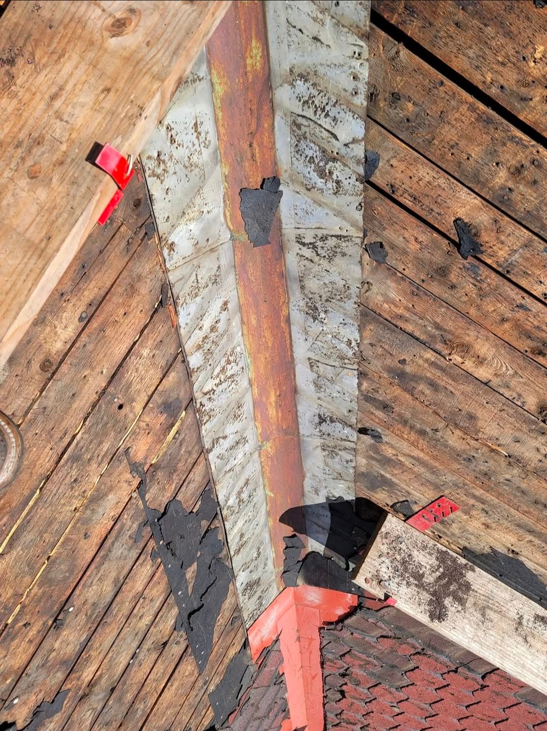 Close-up of a weathered wooden roof with peeling paint and red tape marking damaged areas.