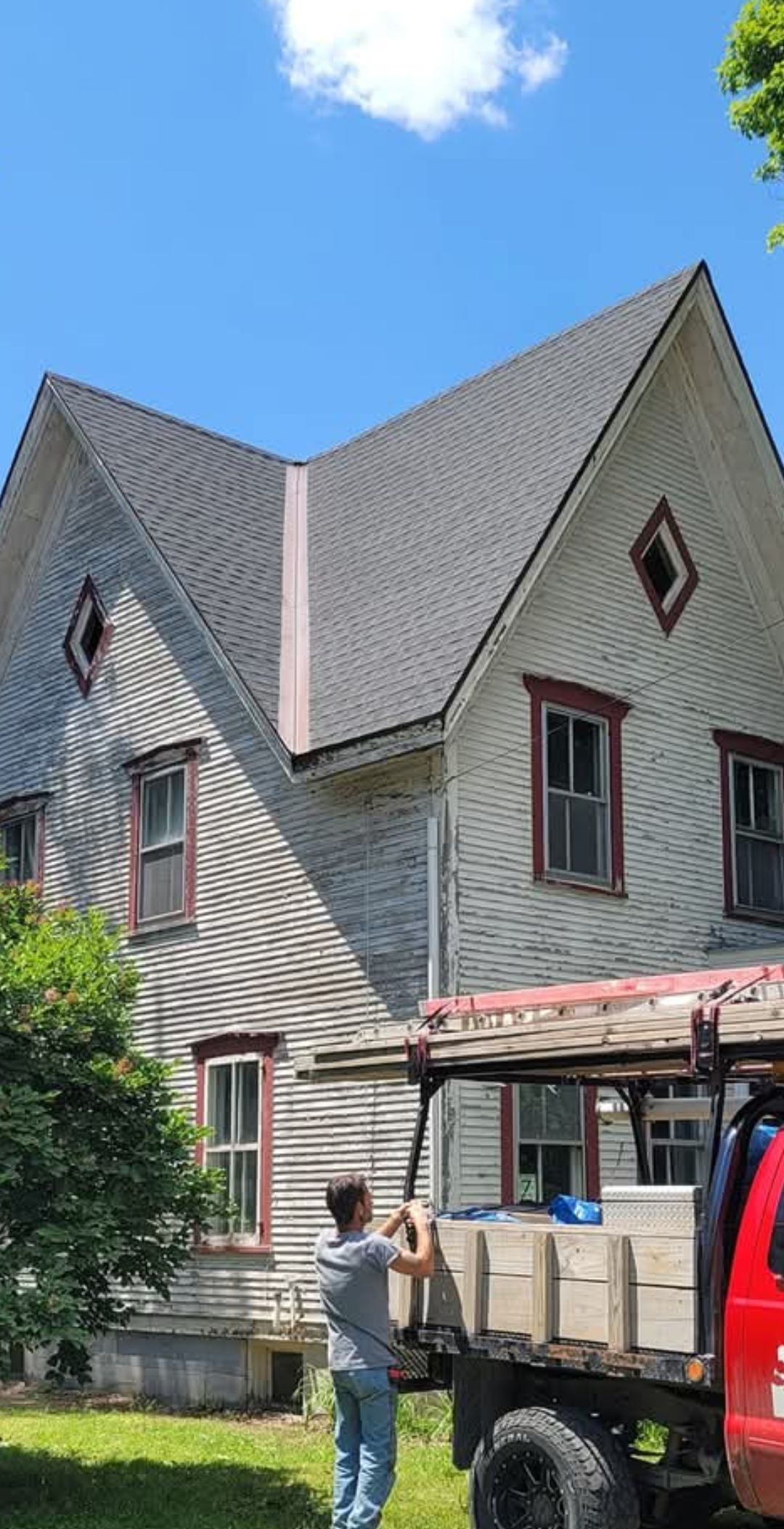 Gray Victorian house with steep gables and striped siding, with a red vehicle and person in front