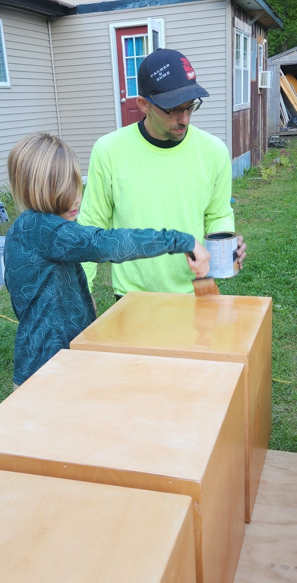 Two people handing a cup over cardboard boxes outdoors near a house