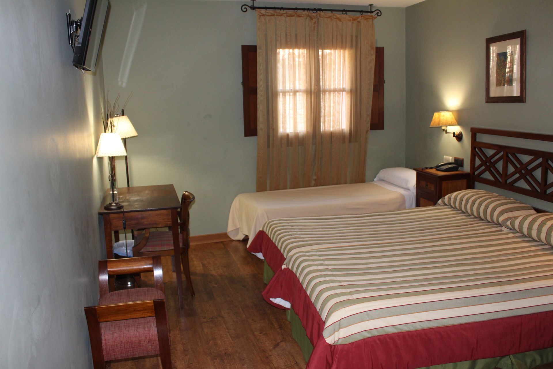 Habitación de hotel con dos camas a rayas, escritorio de madera e iluminación cálida.