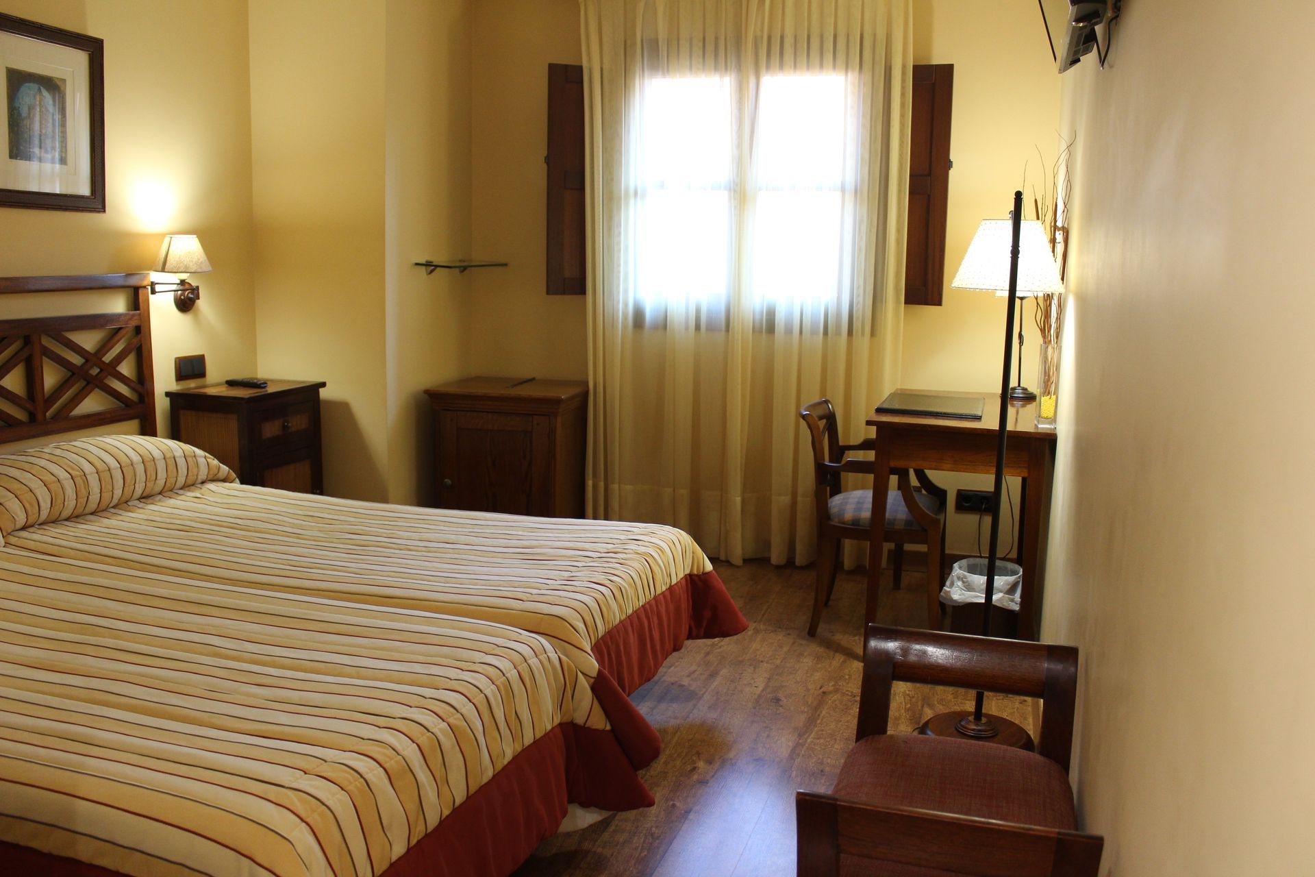 Acogedora habitación de hotel con dos camas individuales, muebles de madera y luz solar cálida que entra por una ventana.
