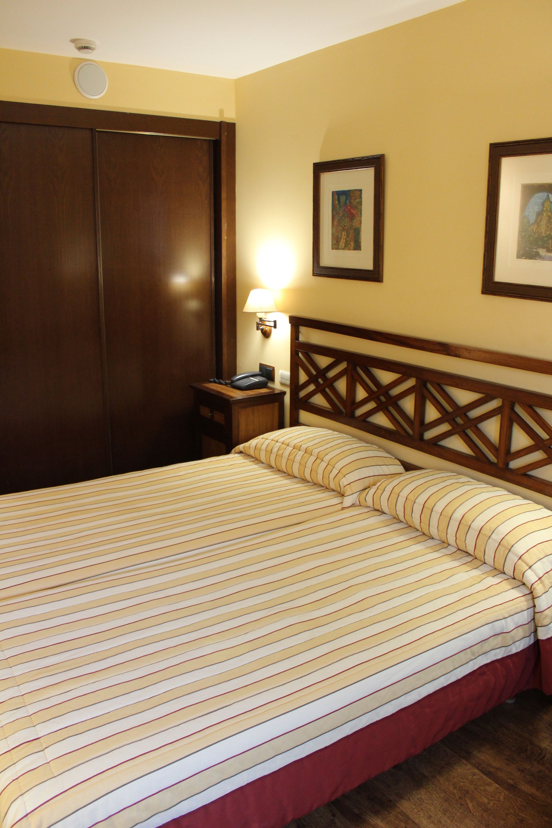Dormitorio con una cama a rayas bien hecha, armario de madera, lámpara de noche y cuadros enmarcados en la pared.