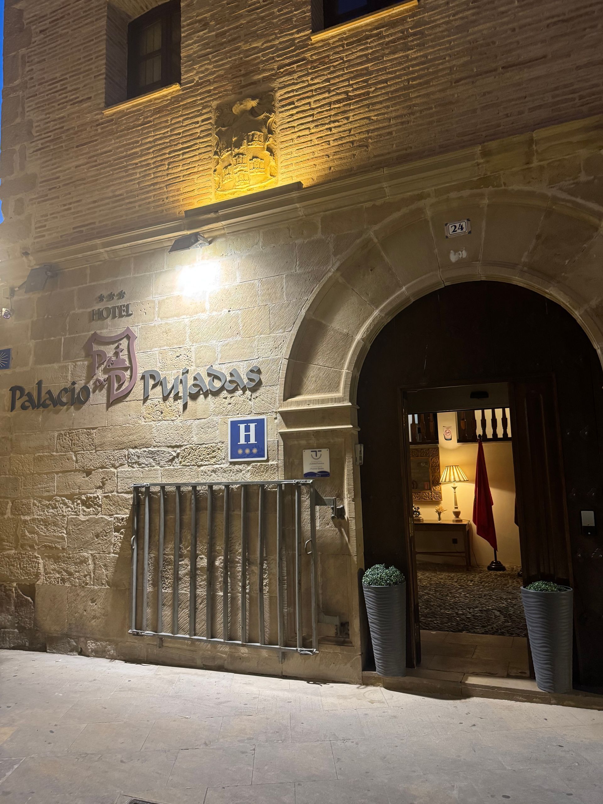 Fachada de piedra iluminada por la noche, con entrada arqueada y letrero 