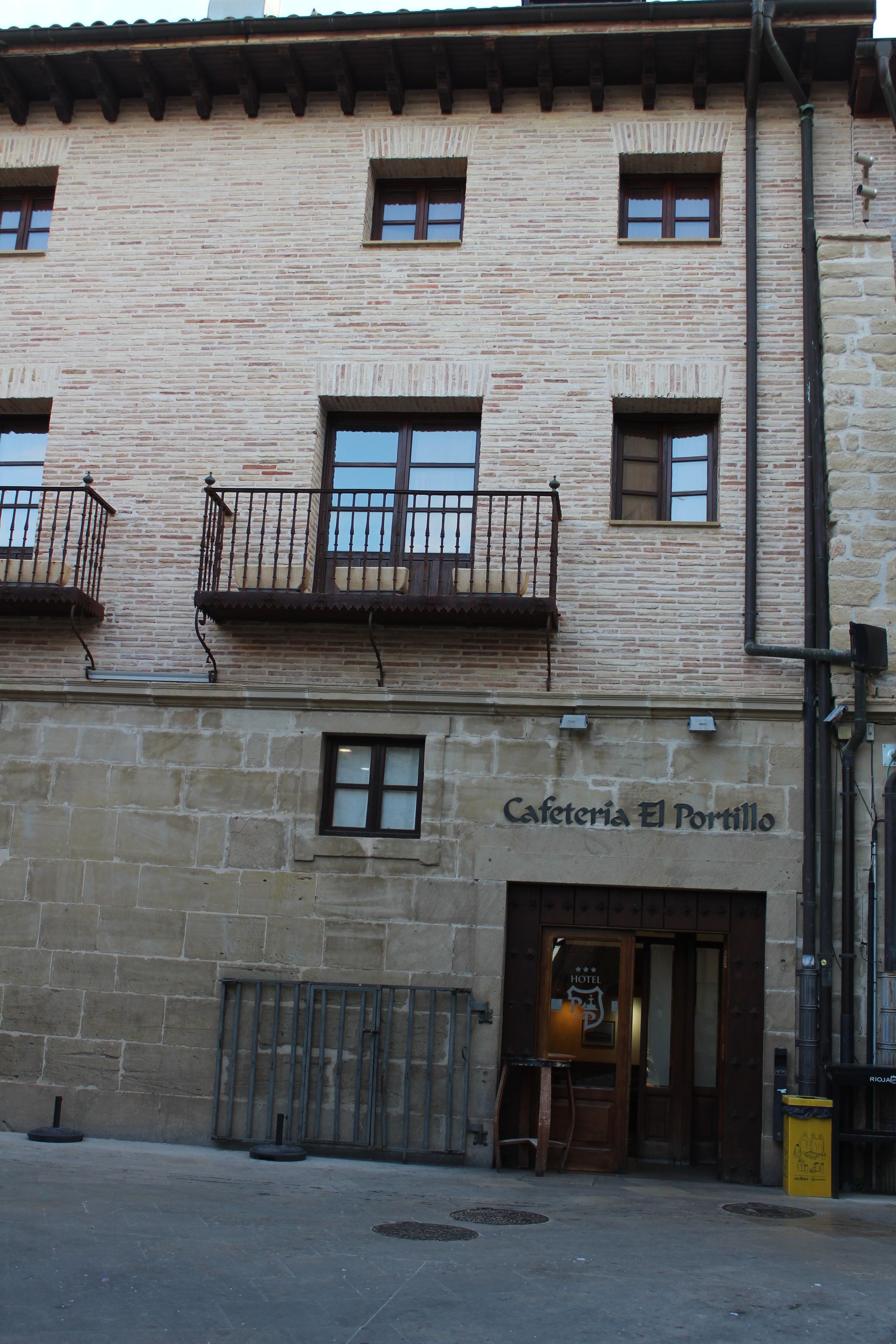 Stone building exterior with balconies and a café entrance, sign reading “Cafetería Porrón”