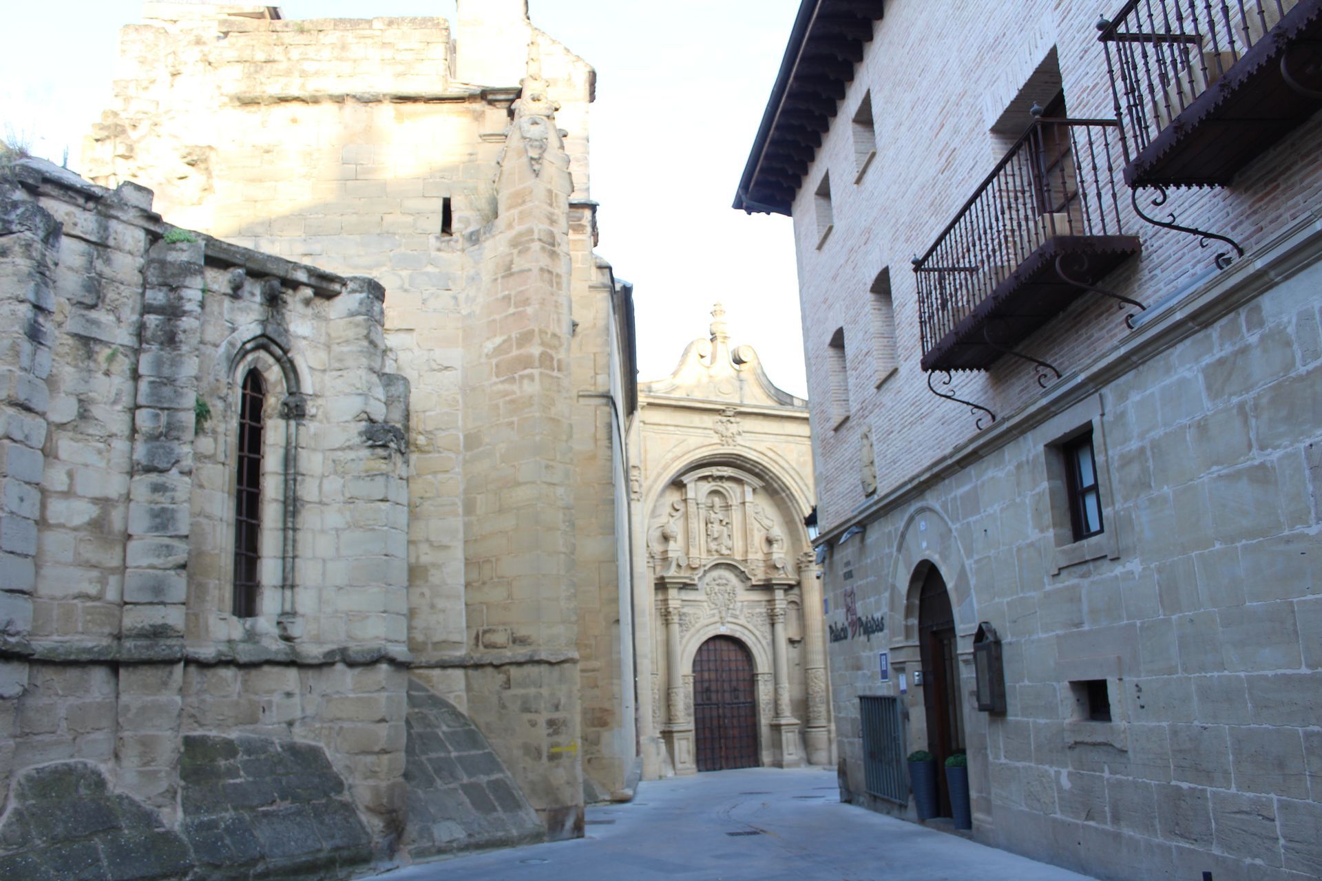 Calle estrecha de piedra que conduce a la entrada de una iglesia con arcos ornamentados, situada entre edificios antiguos.