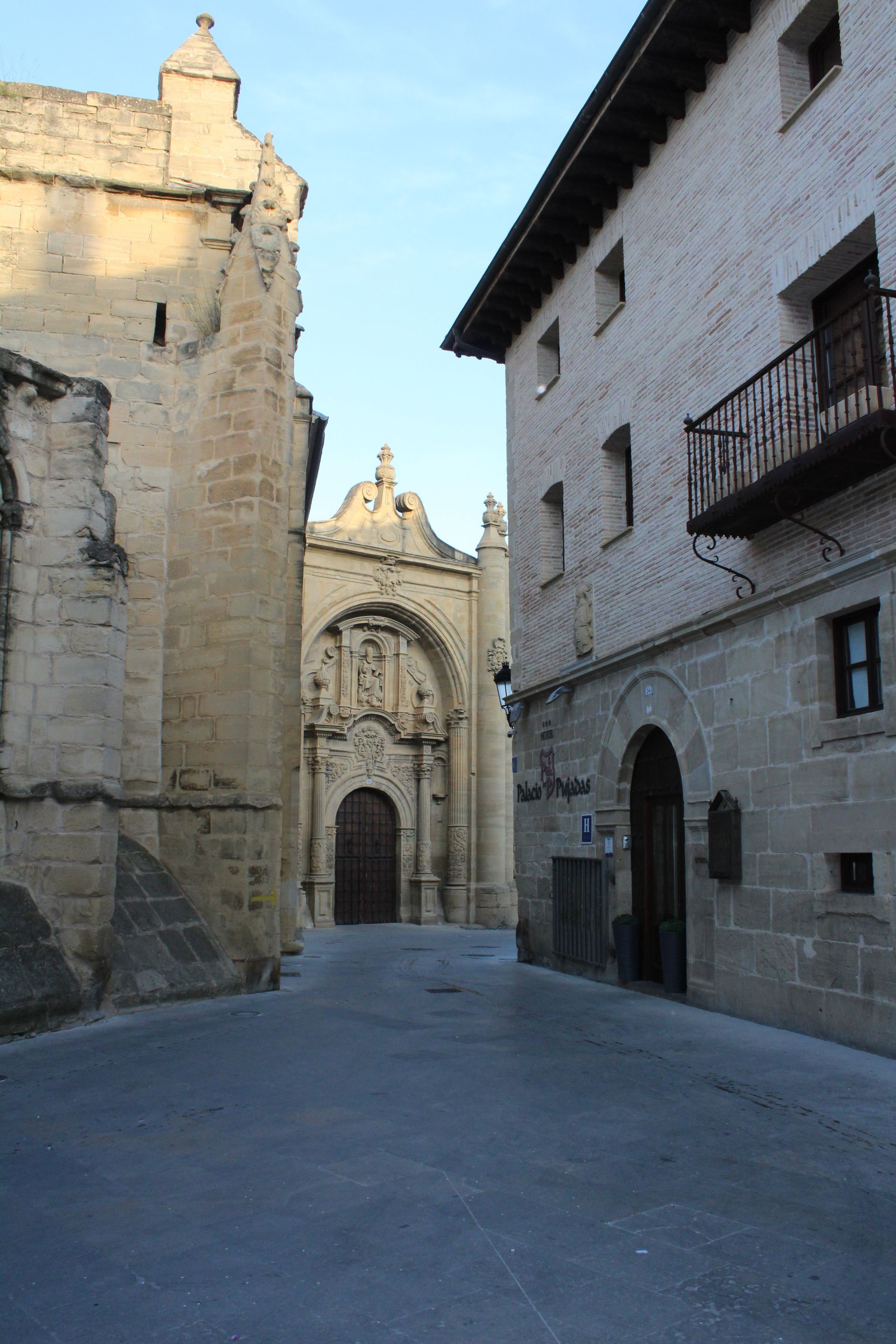 Calle estrecha empedrada junto a edificios antiguos que conduce a una fachada de iglesia con arcos ornamentados.