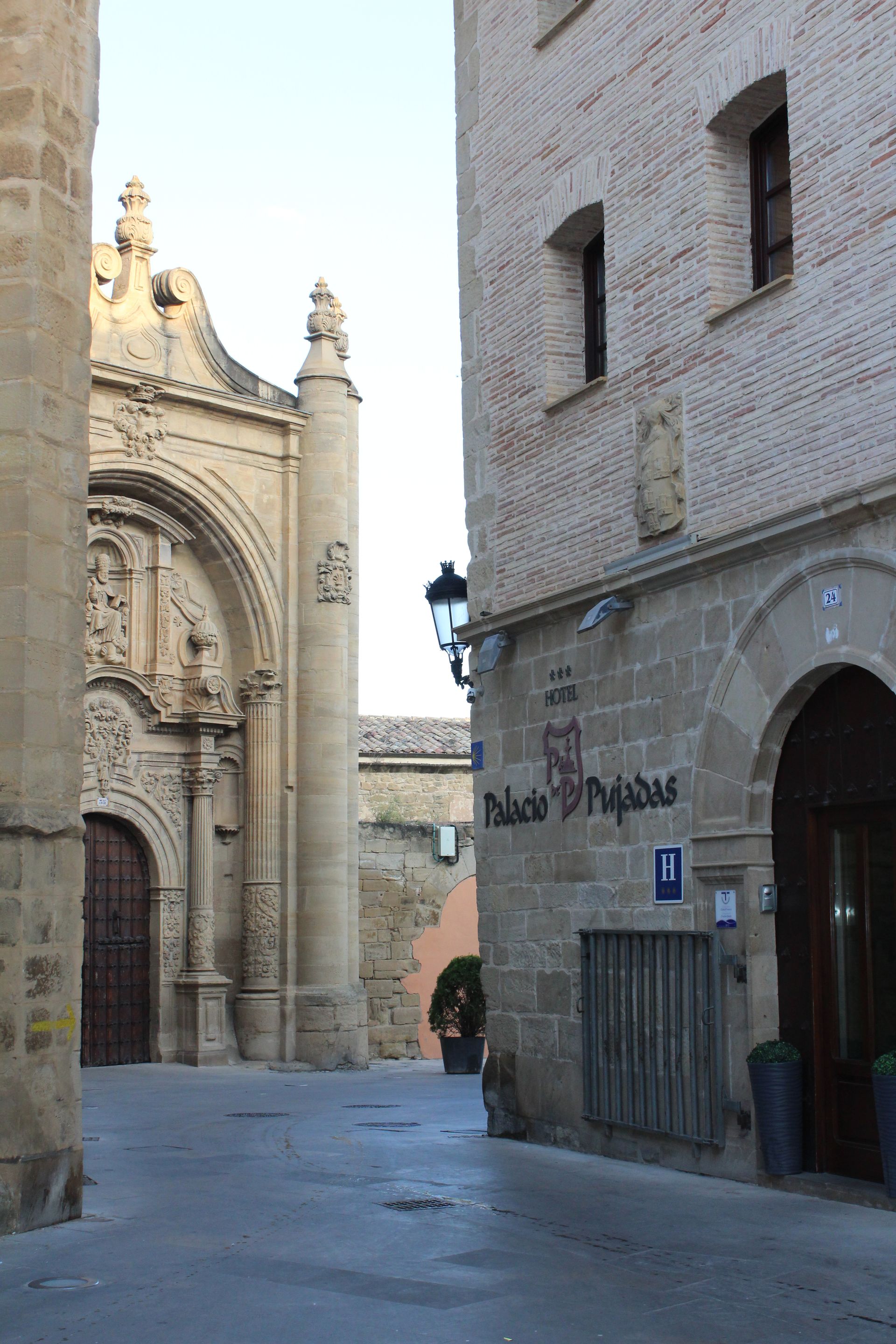 Calle estrecha empedrada entre edificios históricos, con una fachada de iglesia ornamentada a la izquierda.