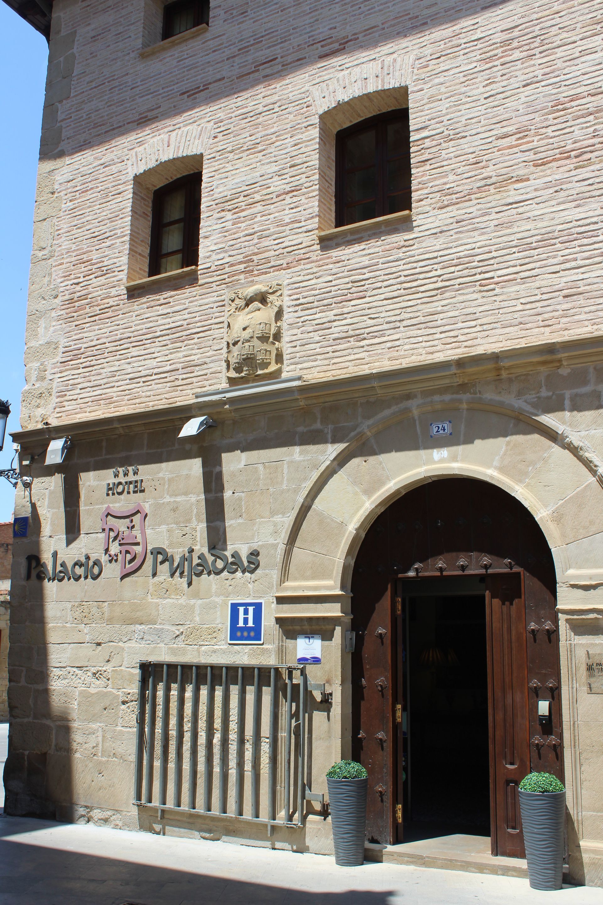 Edificio histórico de ladrillo con puerta de madera arqueada, ventanas pequeñas y un letrero en la pared.