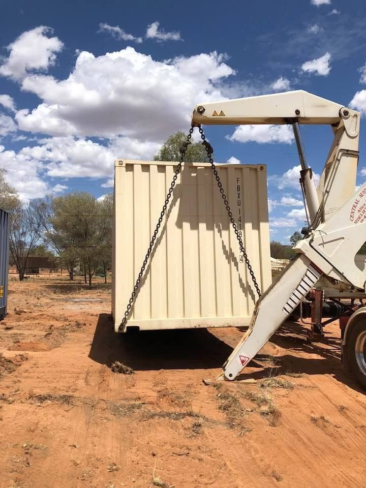 A White Container Is Being Lifted by A Crane in A Dirt Field — Spinifex Container Solutions In Ciccone, NT