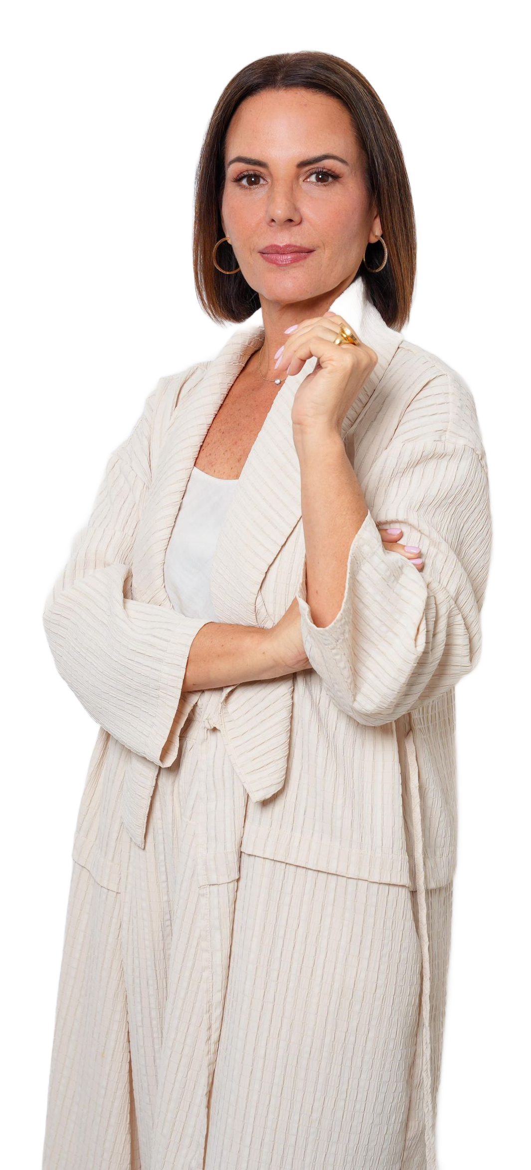 A woman wearing a cream-coloured textured cardigan and dress, standing with her arms crossed against a light grey background.