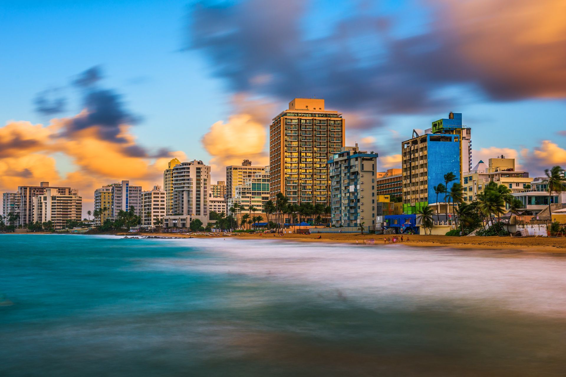 Puerto Rico skyline at sunset beside a turquoise beach with blurred waves and colorful clouds