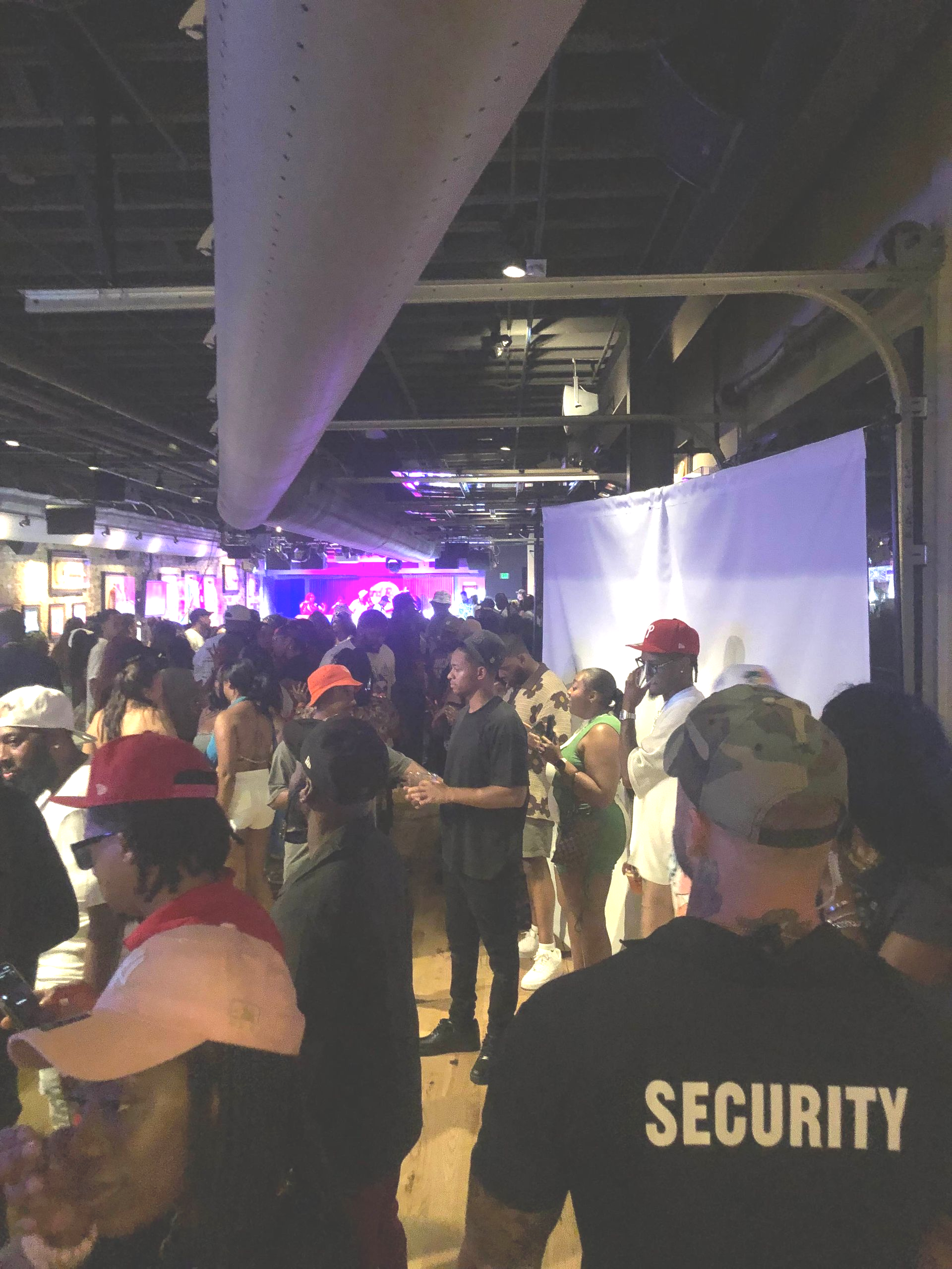 Crowd at an event in an industrial space. Security guard in foreground. People gathered with purple lighting.