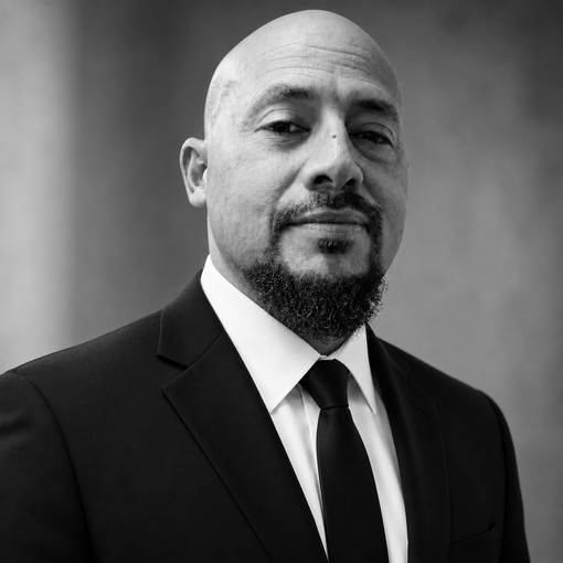 Black-and-white studio portrait of a man in a suit and tie with a neutral expression