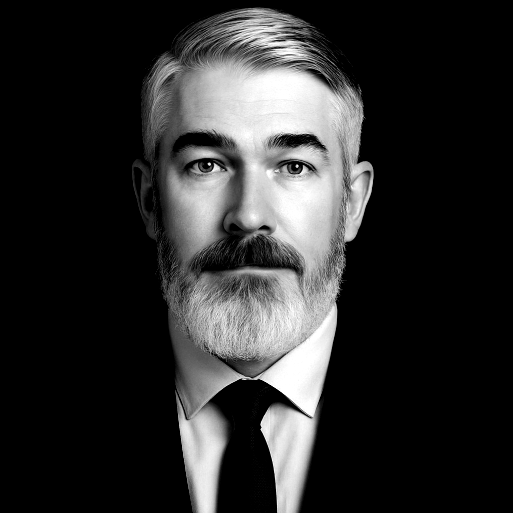 Black and white portrait of a man with a gray beard, wearing a suit and tie, looking at the viewer.