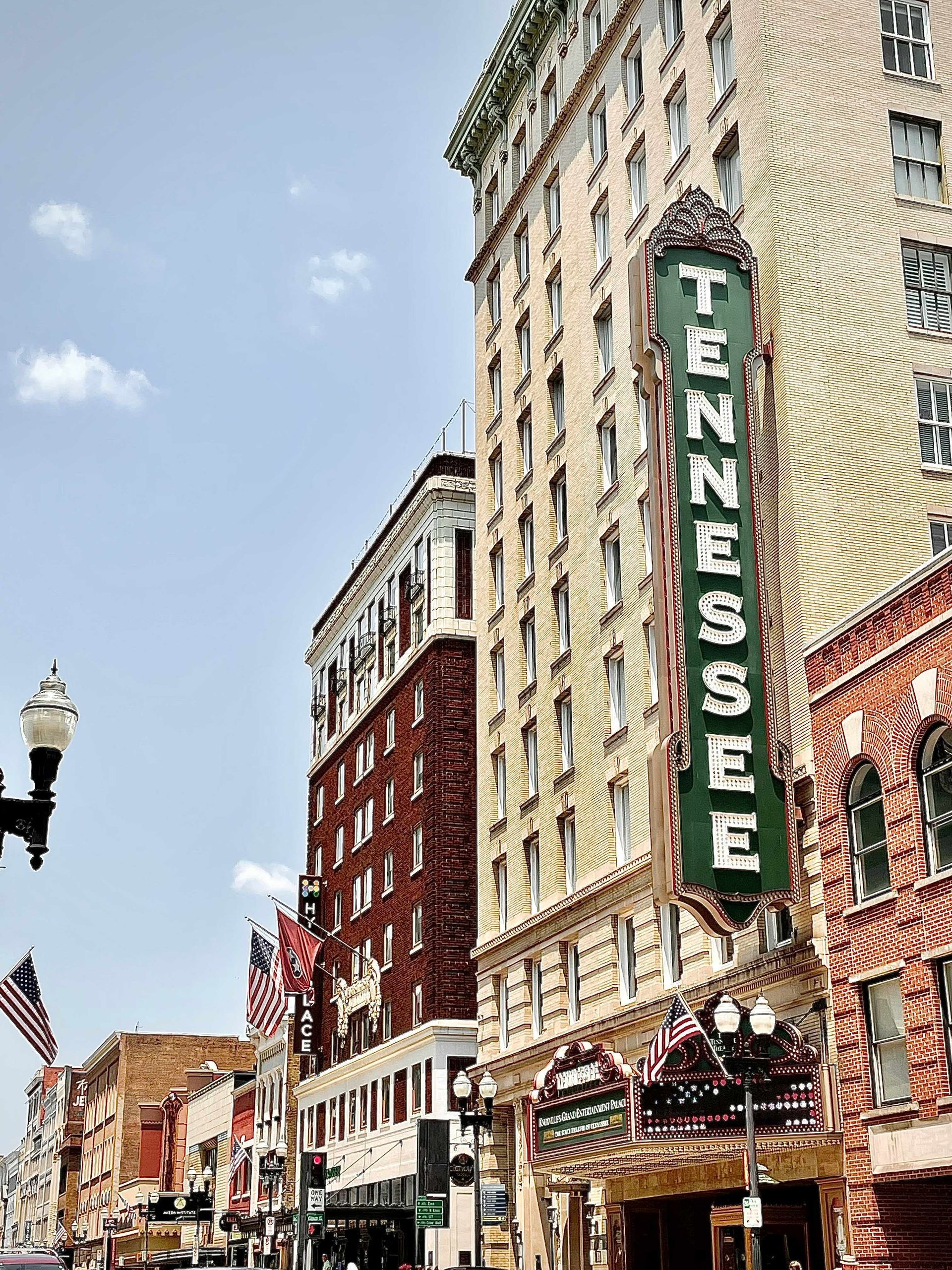 Tennessee Theatre sign on a tall brick building in a downtown street setting, flags, blue sky.
