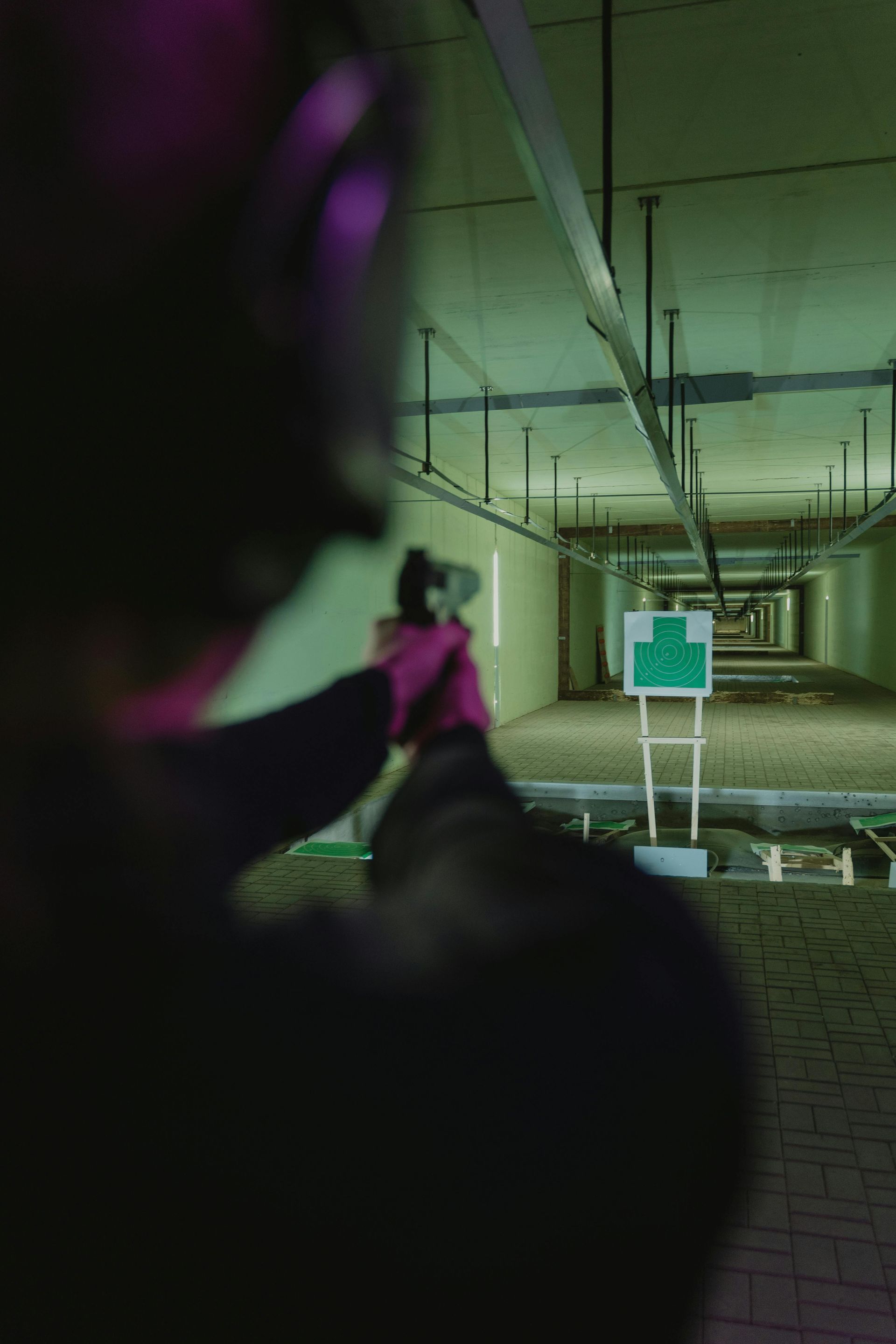 Person aiming a handgun at a target in a shooting range. Green and purple lighting.