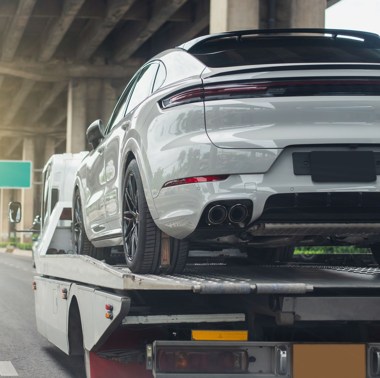 White sports car on a tow truck under an overpass