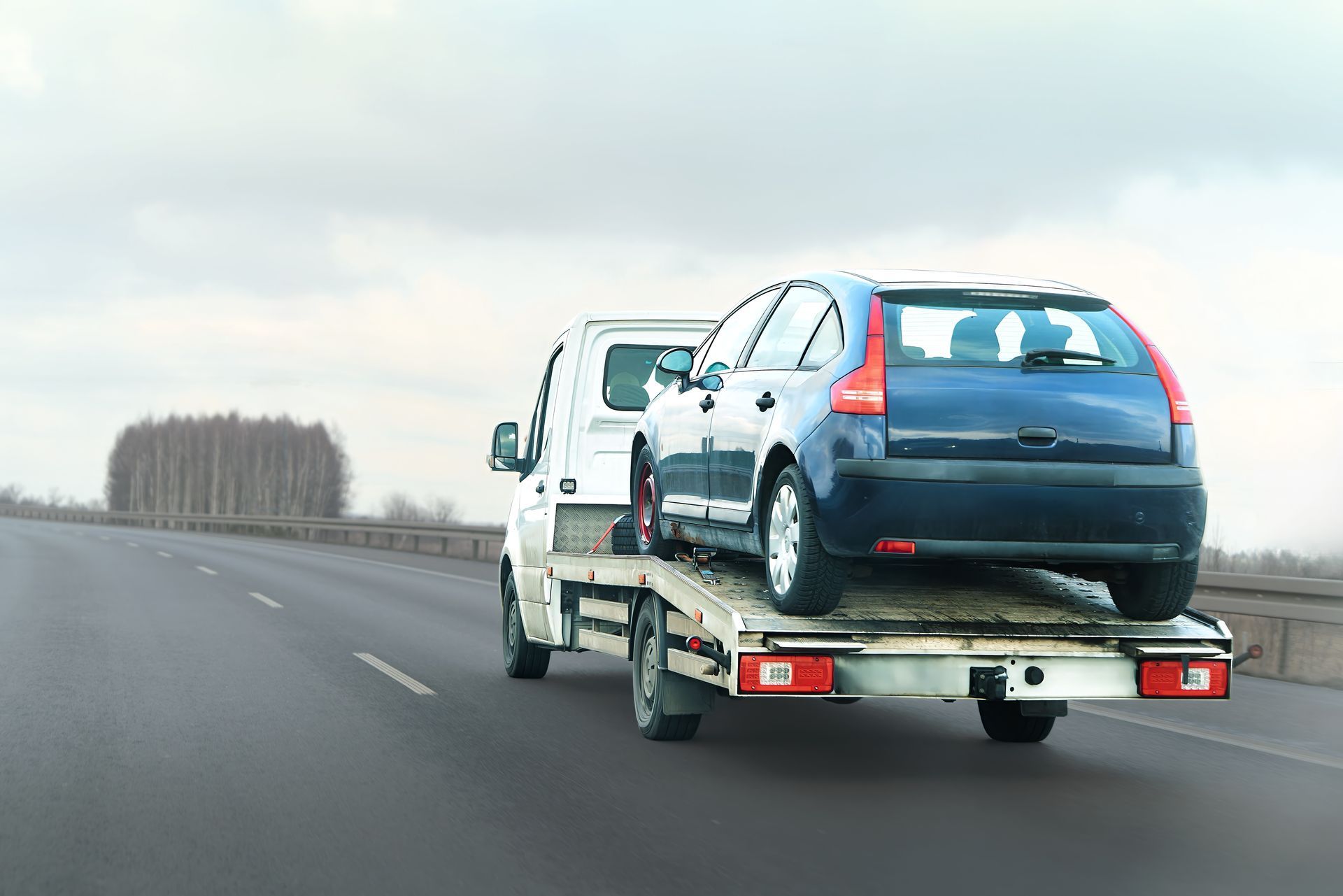 Tow truck hauling a blue car on a highway