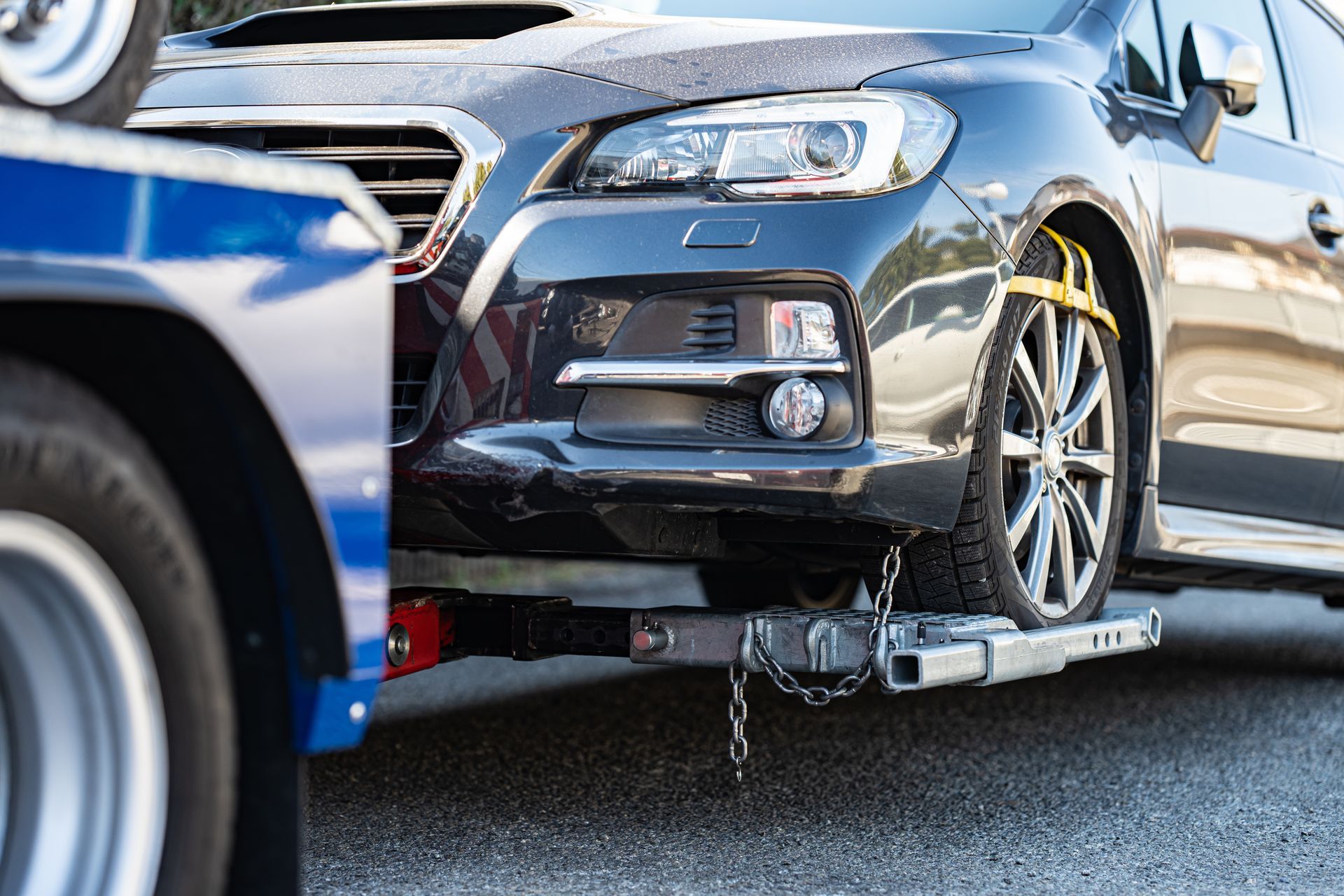 Black car being towed on a flatbed truck after a collision, with a damaged blue vehicle in front