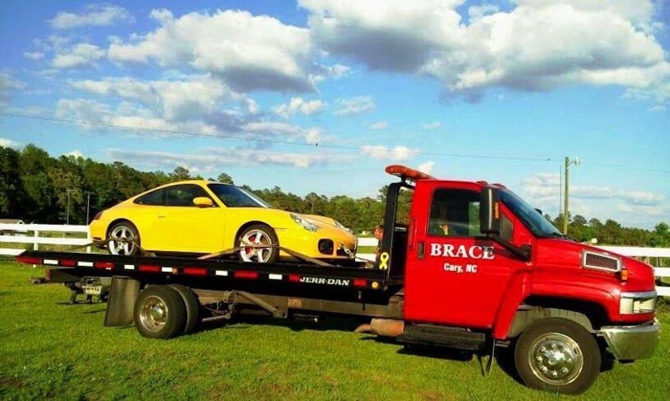 Red tow truck hauling a yellow sports car on a flatbed in a grassy field