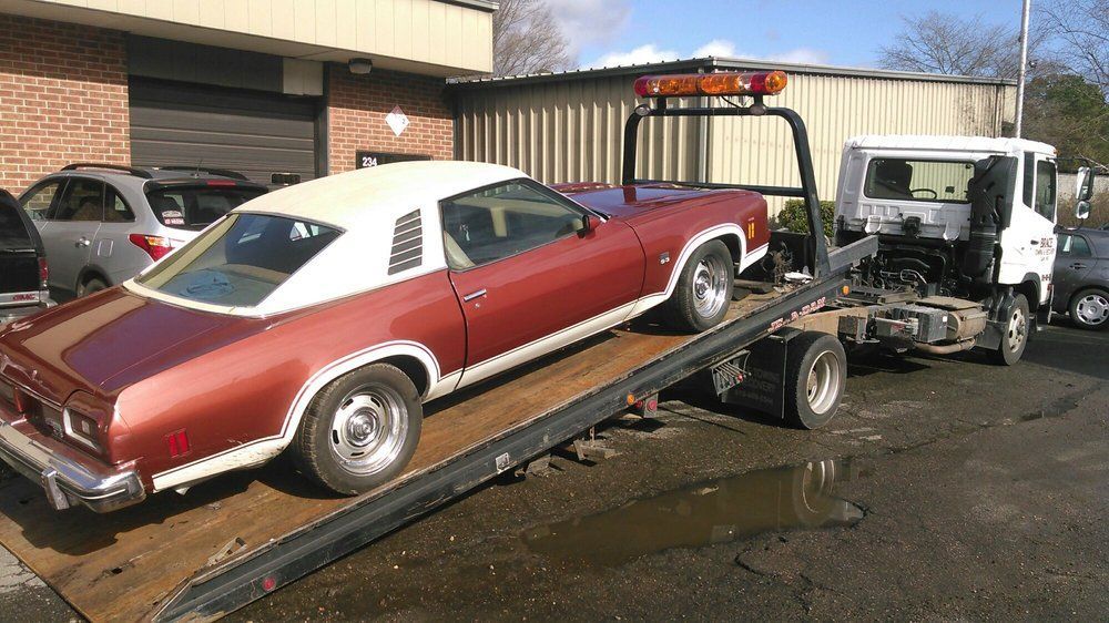 Red classic car on a tow truck trailer behind a white tow truck in a lot