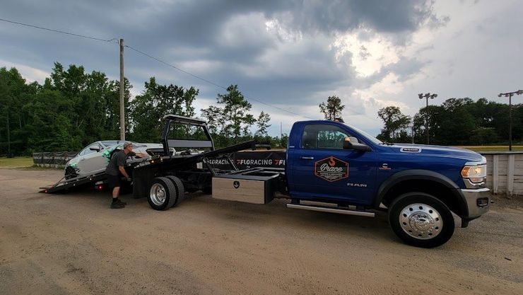 Blue pickup truck towing a trailer with equipment on a dirt road under cloudy skies