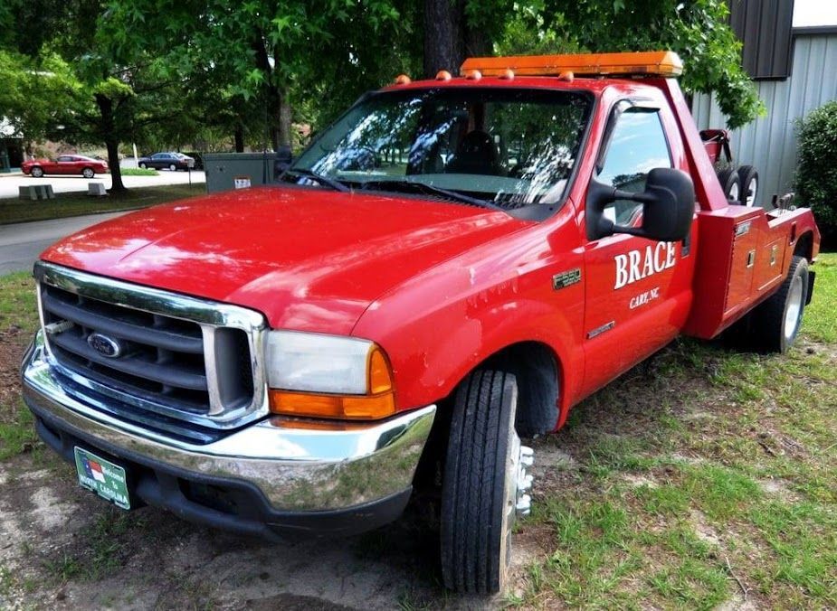 Red tow truck parked on grass beside a building, with orange light bar and company lettering on the door
