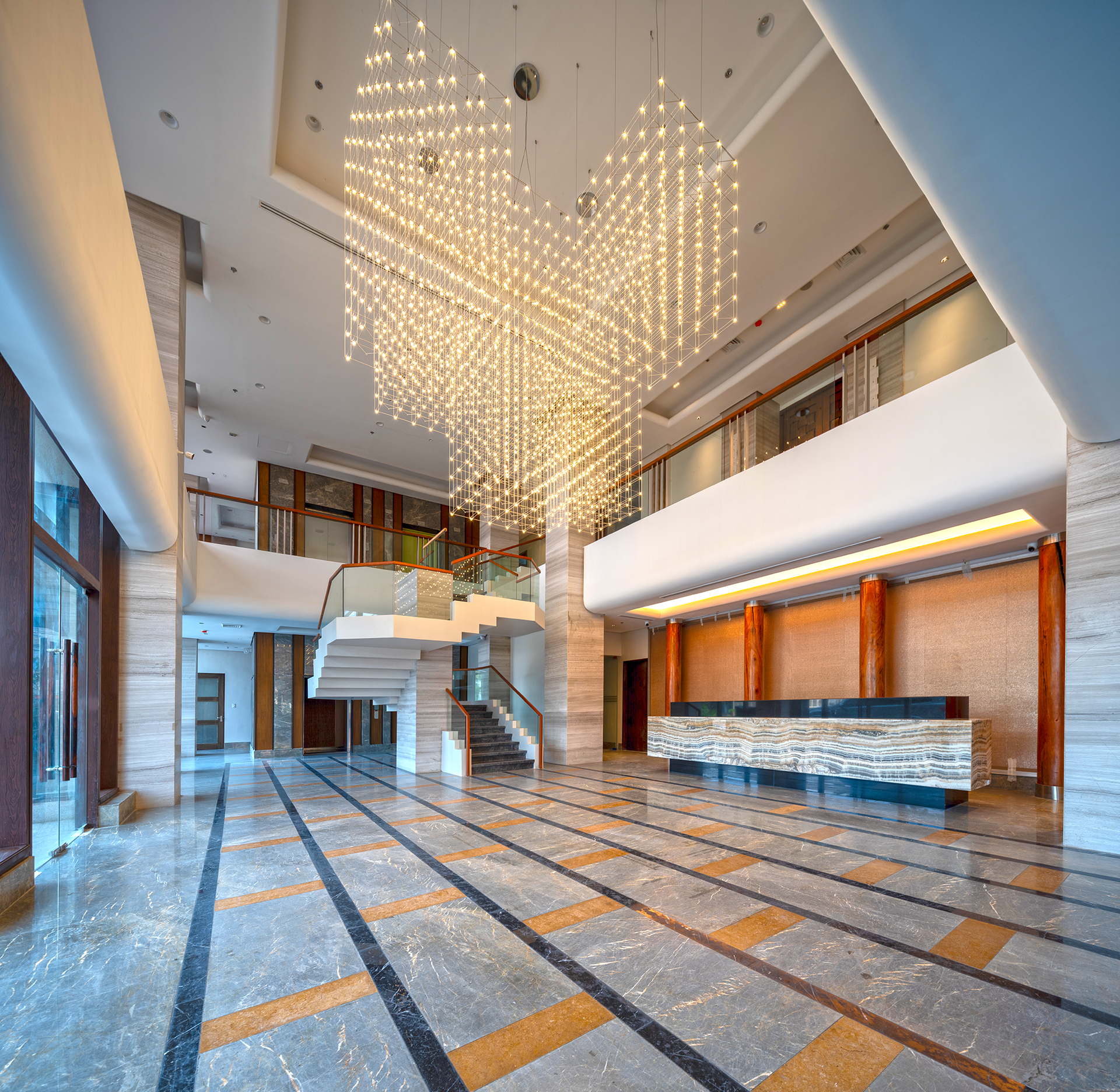 Lobby with marble floors, a grand staircase, and a large chandelier. Reception desk in the distance.