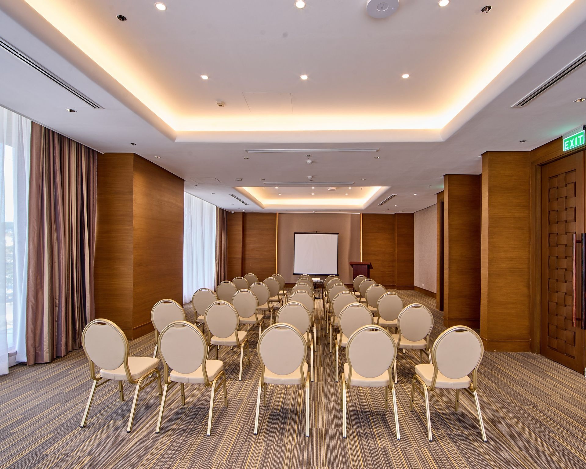 A conference room with beige chairs arranged for a presentation, with a projector screen at the front.